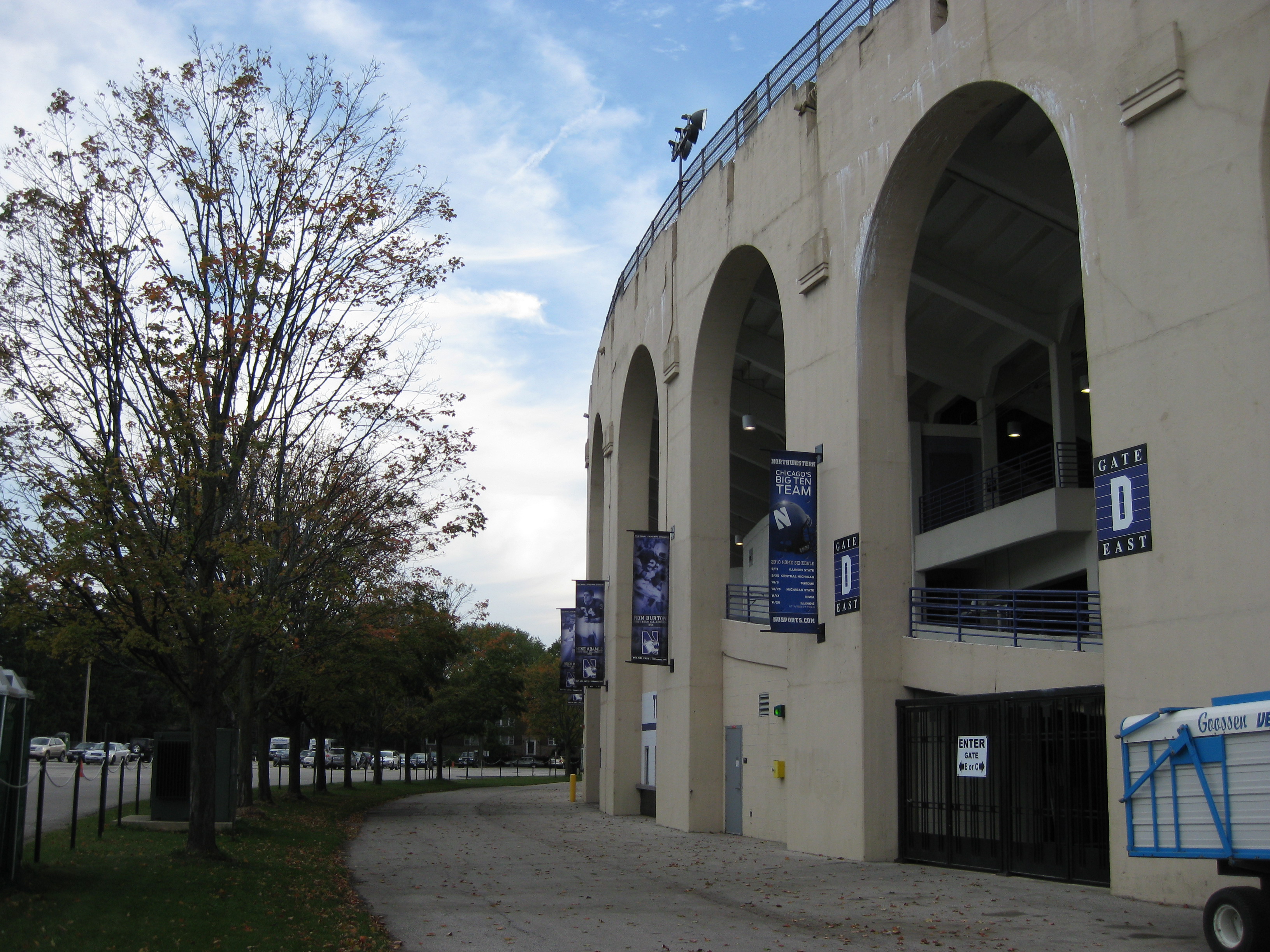 Stadium exterior with arched concrete openings, blue and white banners, and a gate entrance.