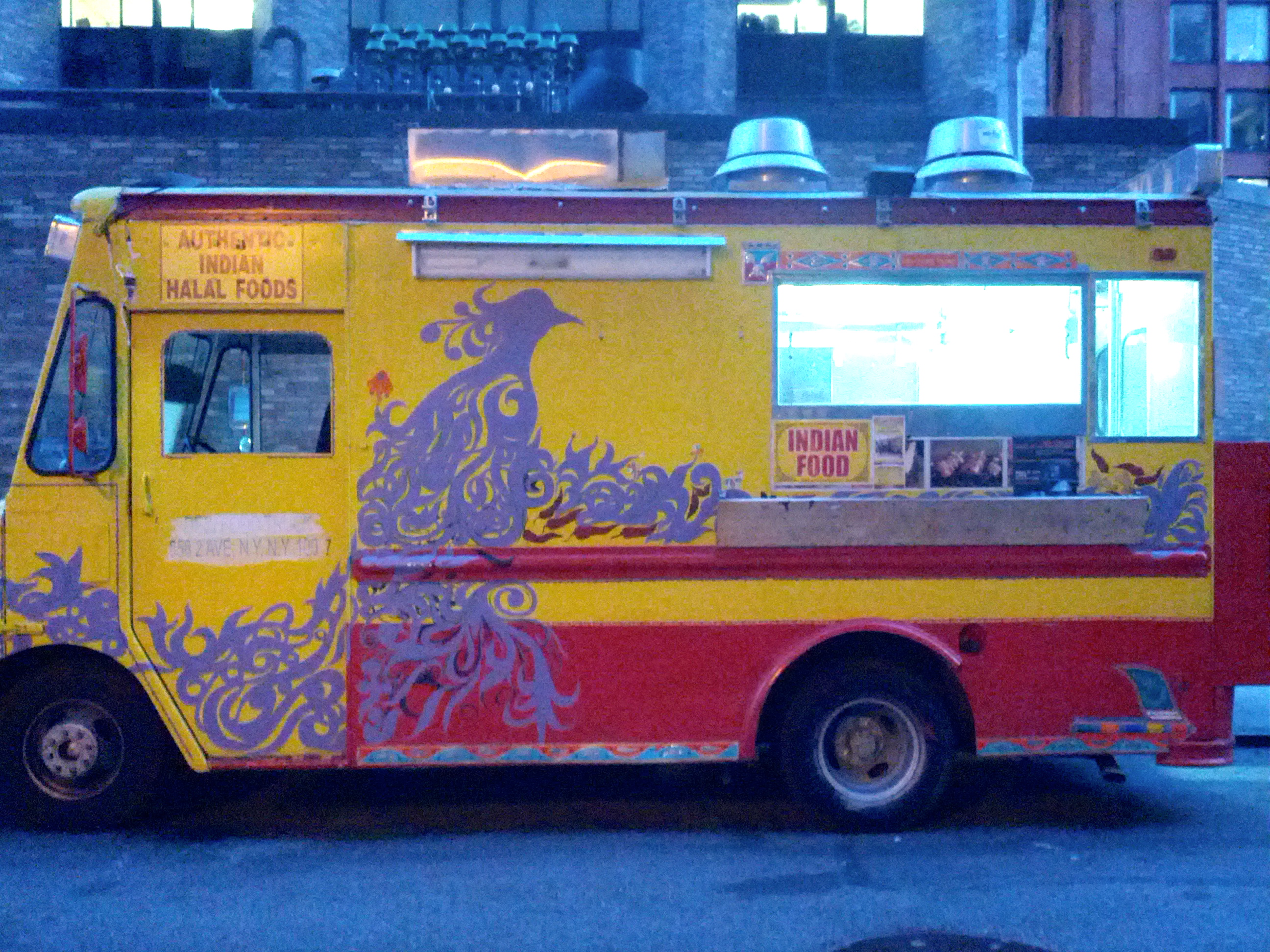 A yellow and red food truck with a peacock design and open service window.