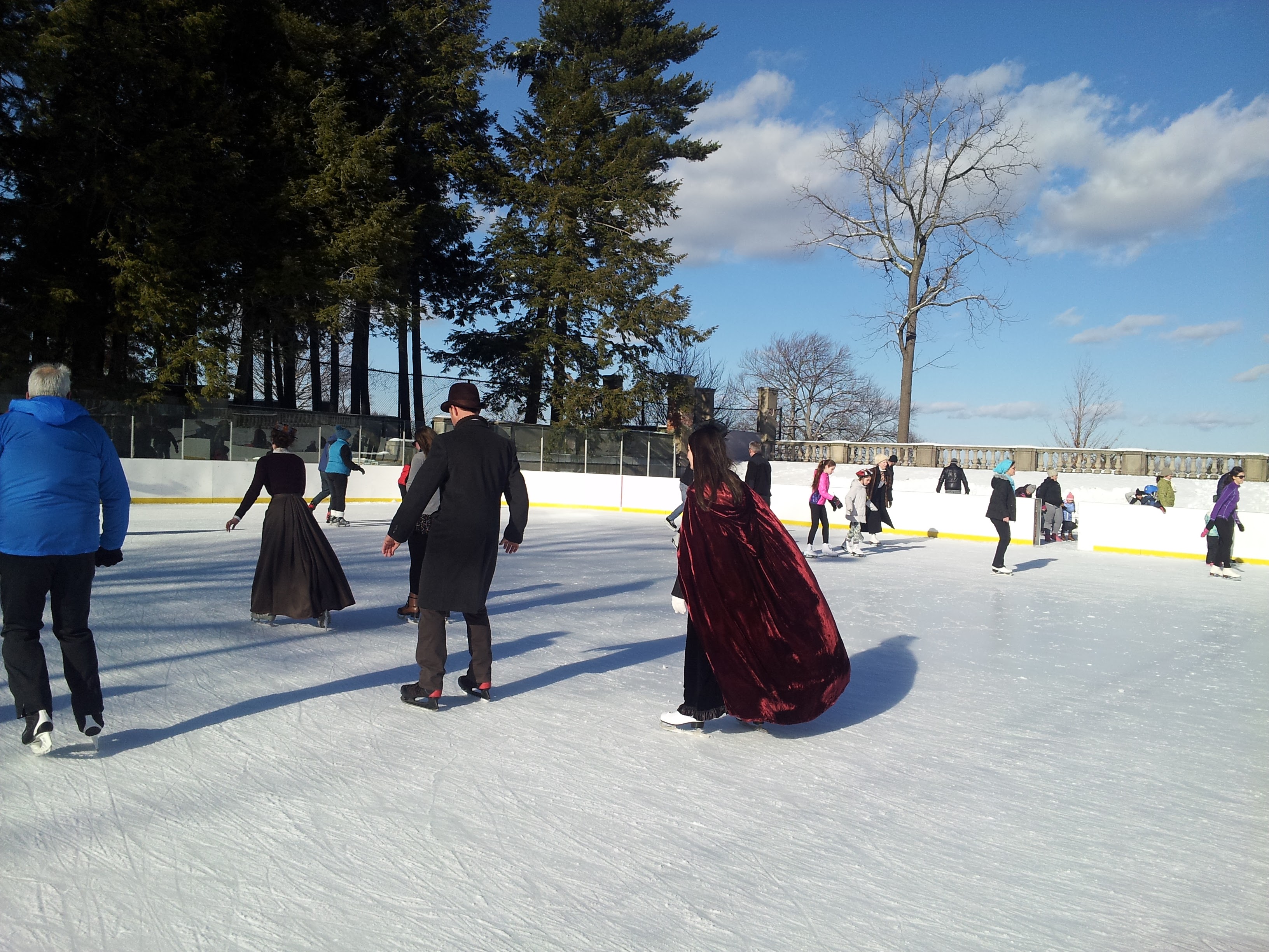 Multiple people ice skating on a sunny outdoor rink in winter