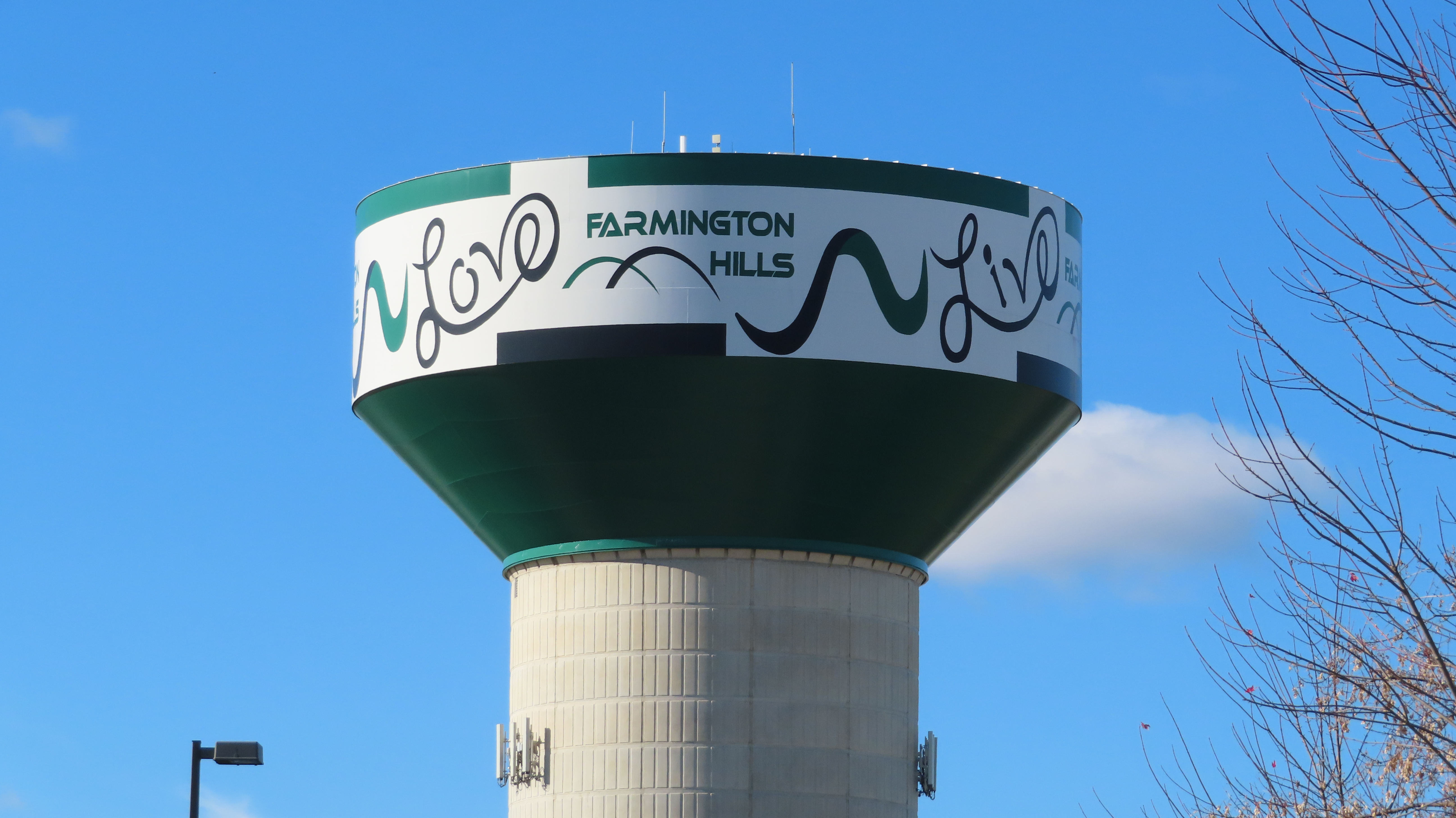 Green and white municipal water tower with city name lettering against a blue sky.