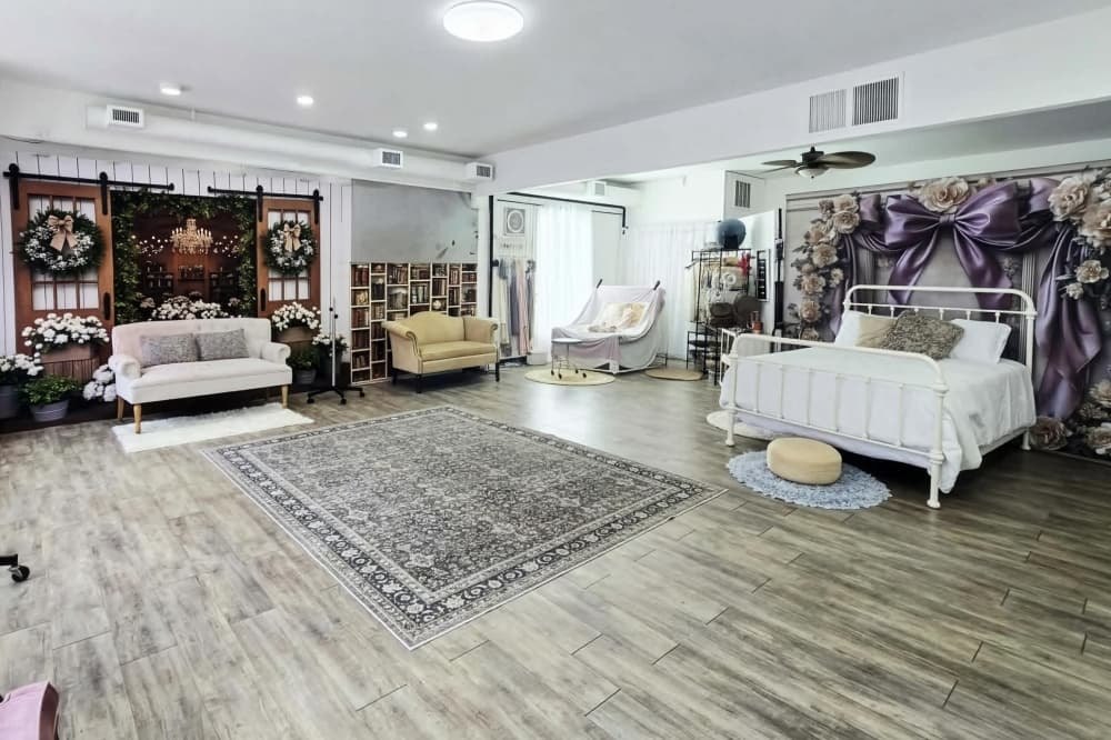 Open photography studio interior with styled sets, floral backdrops, and wood-look flooring.