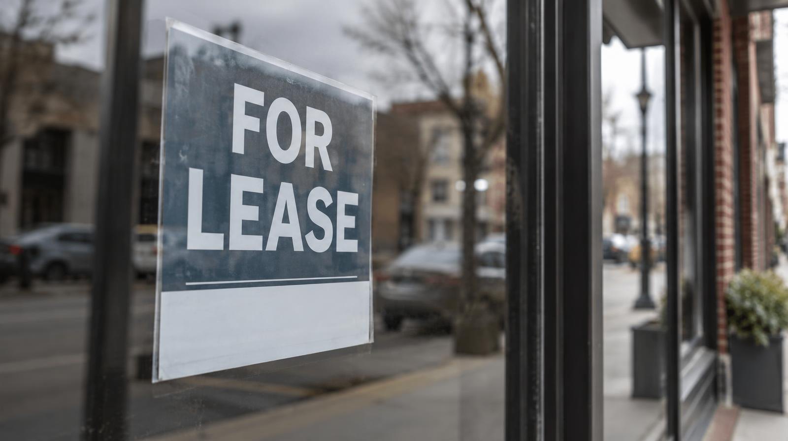Empty shop window with a for lease sign reflecting a city street outside.