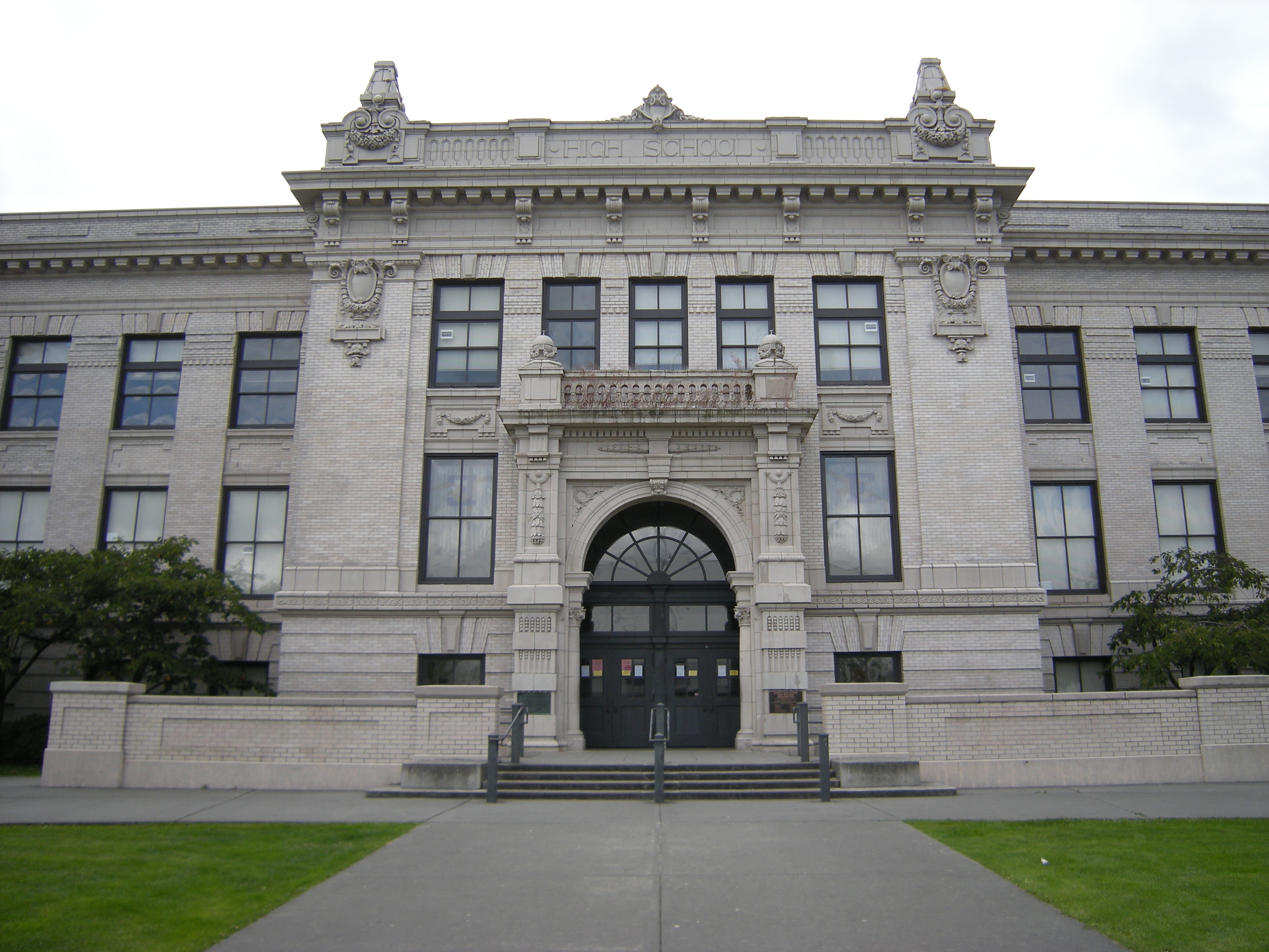 Neoclassical stone facade of Everett High School with arched entrance and green lawn.