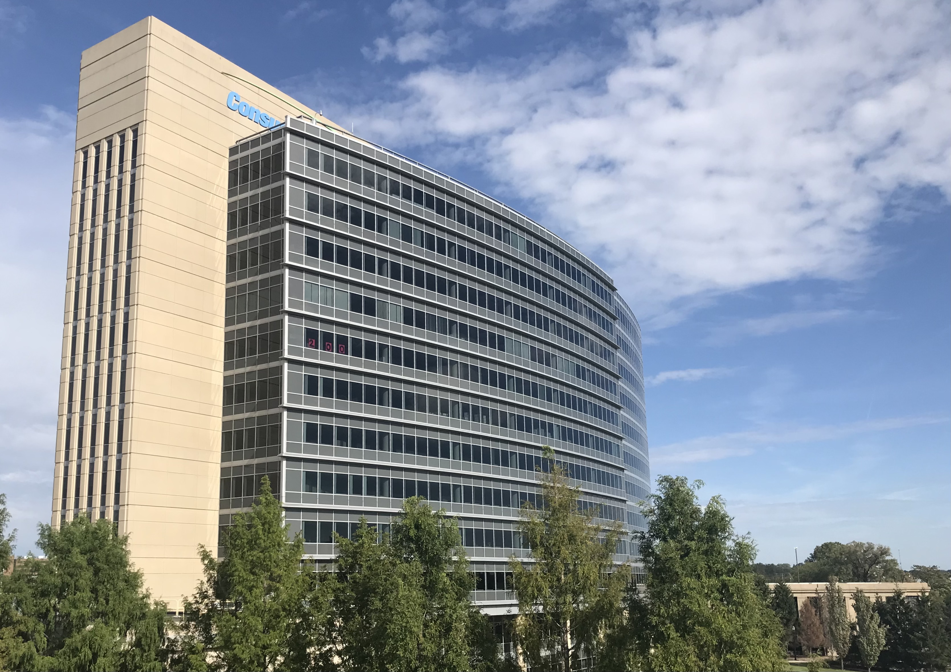 Multi-story curved glass office building with a Consumers Energy logo near the roofline.