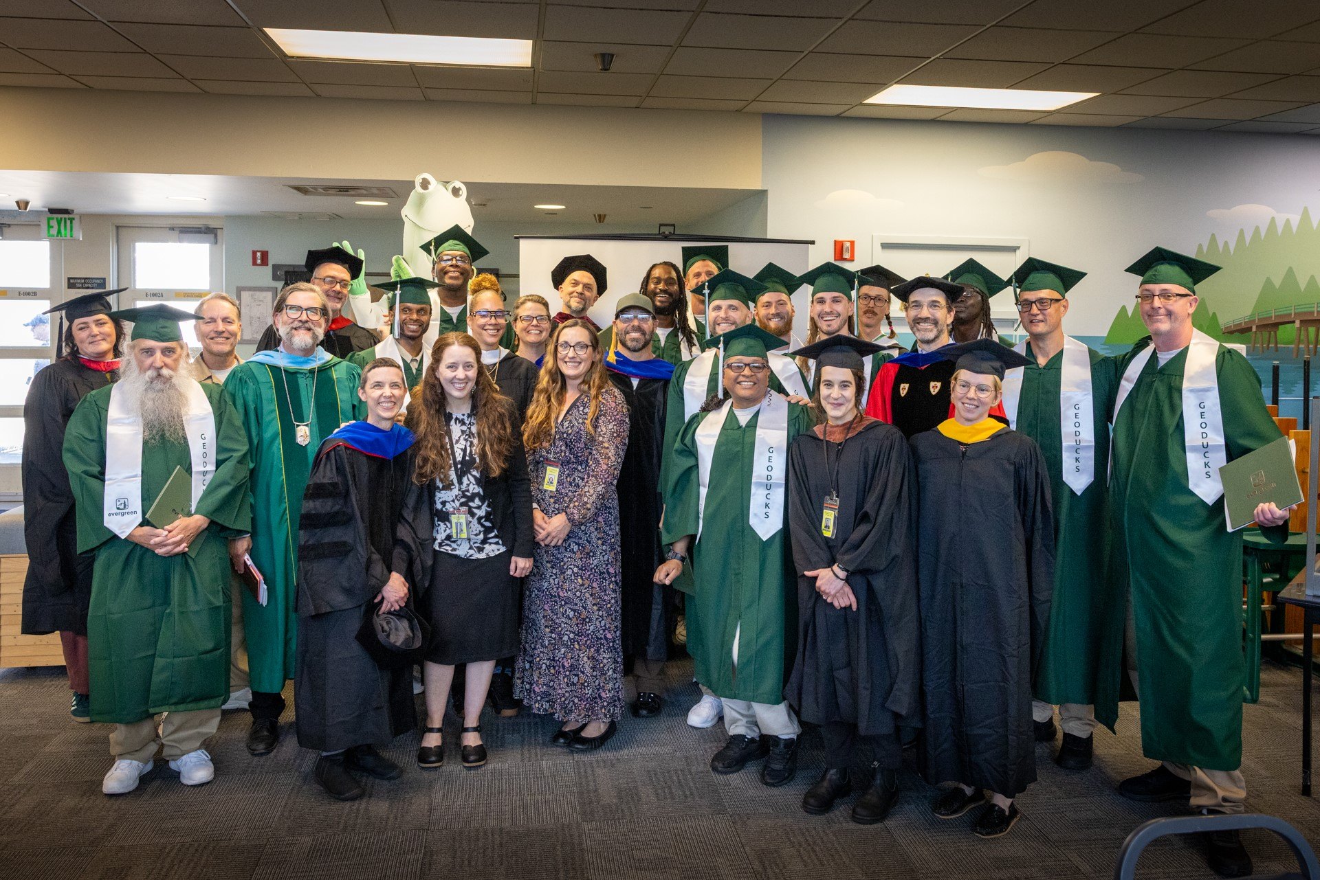 Group of people in green graduation caps and gowns posing indoors.