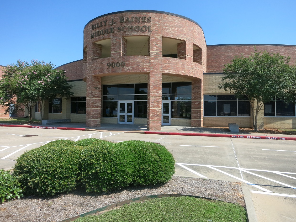 Brick school building with curved entrance tower and empty parking lot under blue sky.
