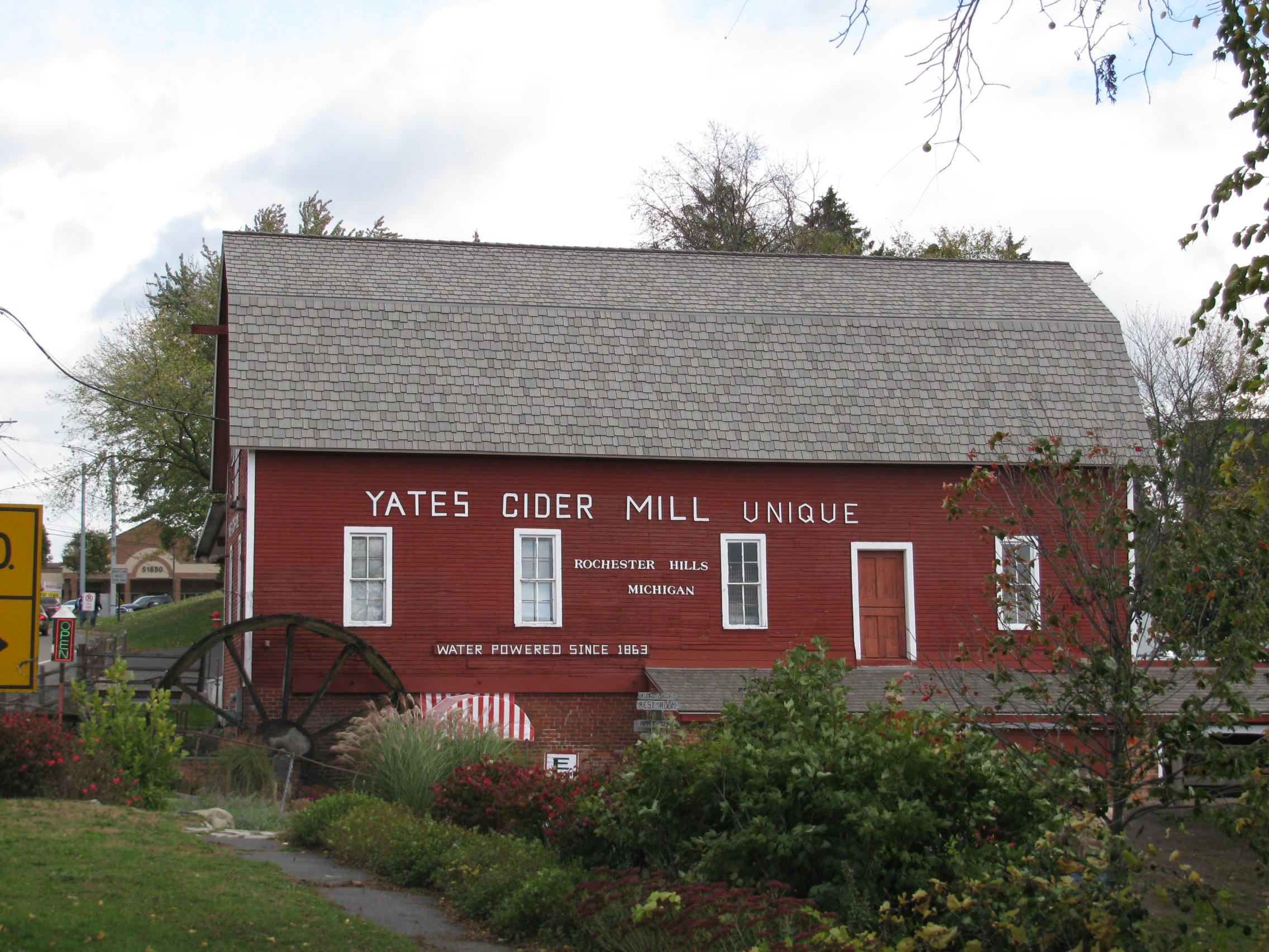 Red barn building with water wheel reading 'Yates Cider Mill' surrounded by autumn trees.