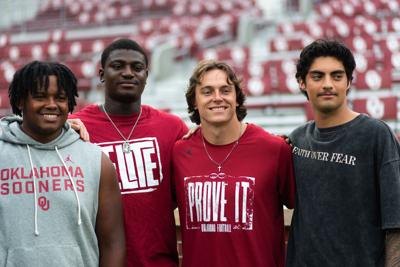 Four young men in Oklahoma Sooners athletic gear pose together in a stadium.