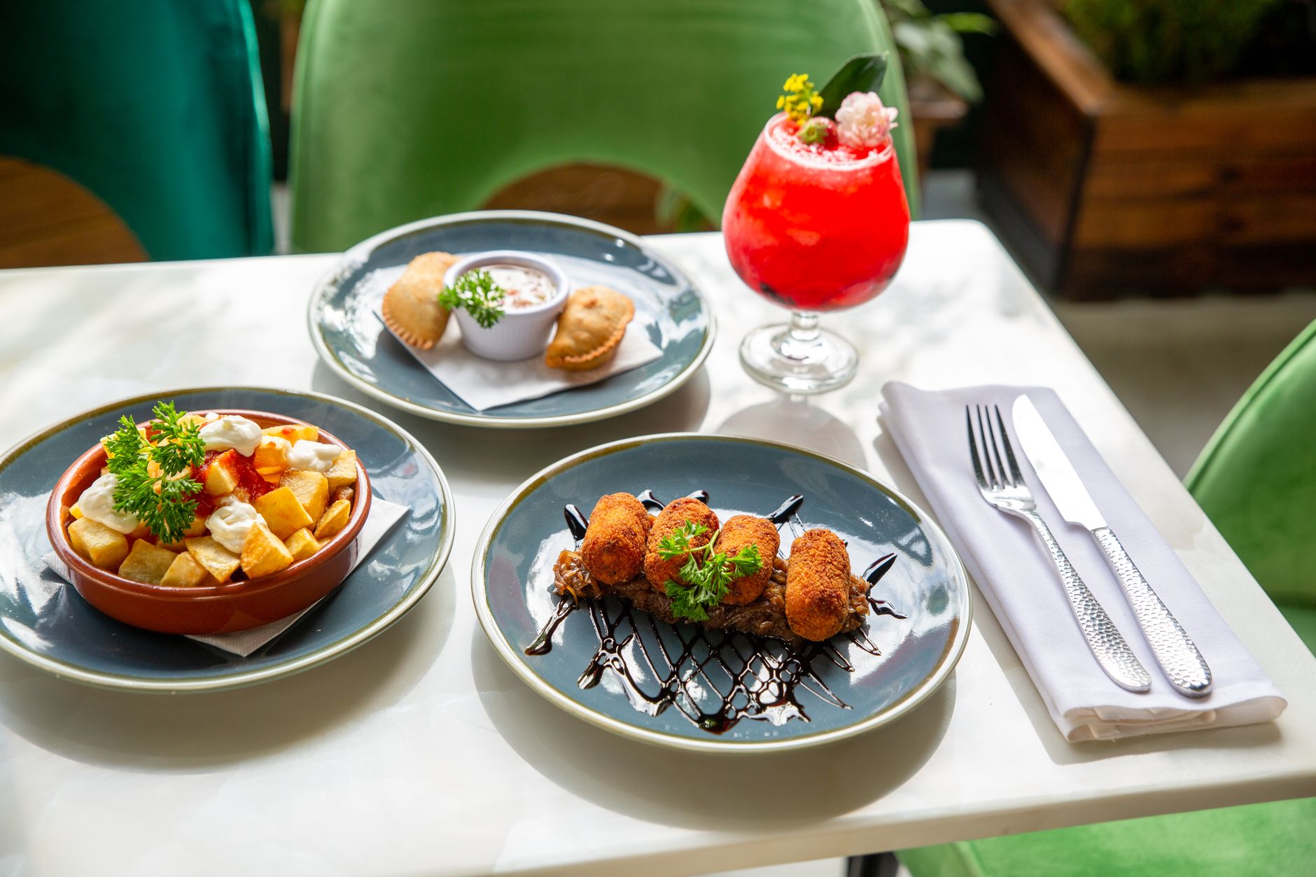 A vibrant spread of Spanish tapas dishes paired with a refreshing cocktail on a sunlit table.