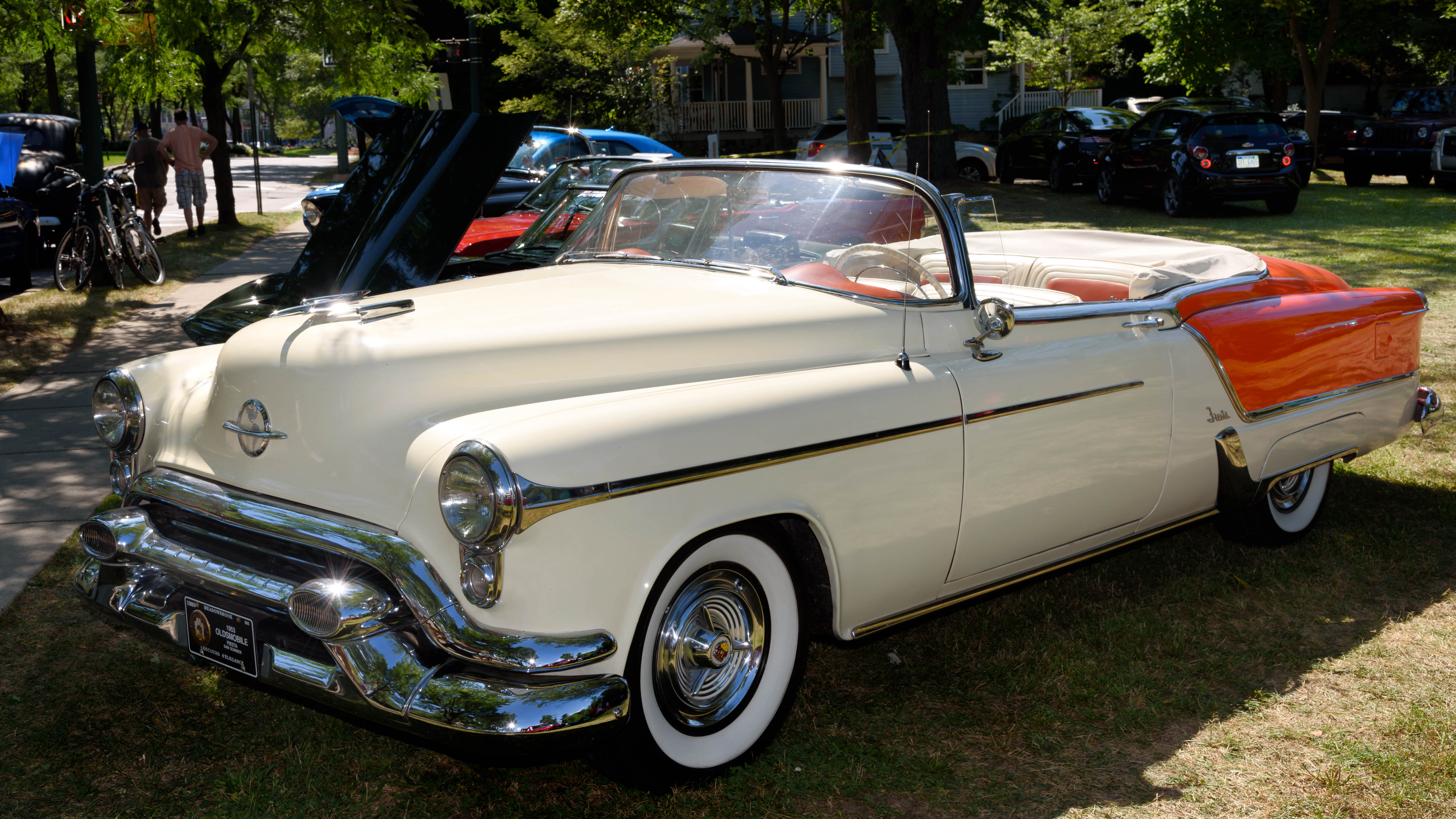 Cream and orange vintage convertible with whitewall tires at an outdoor car show.