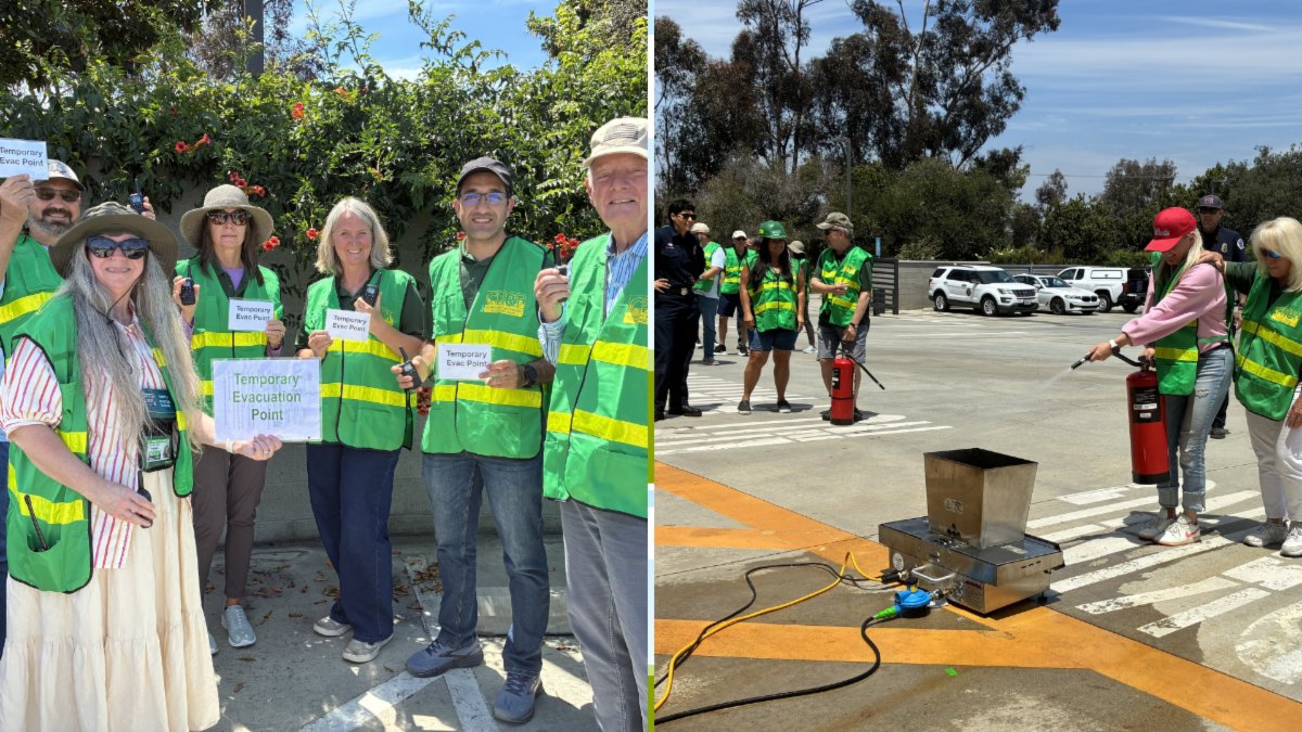 People in green safety vests watch a fire extinguisher demonstration on a small controlled fire outdoors.