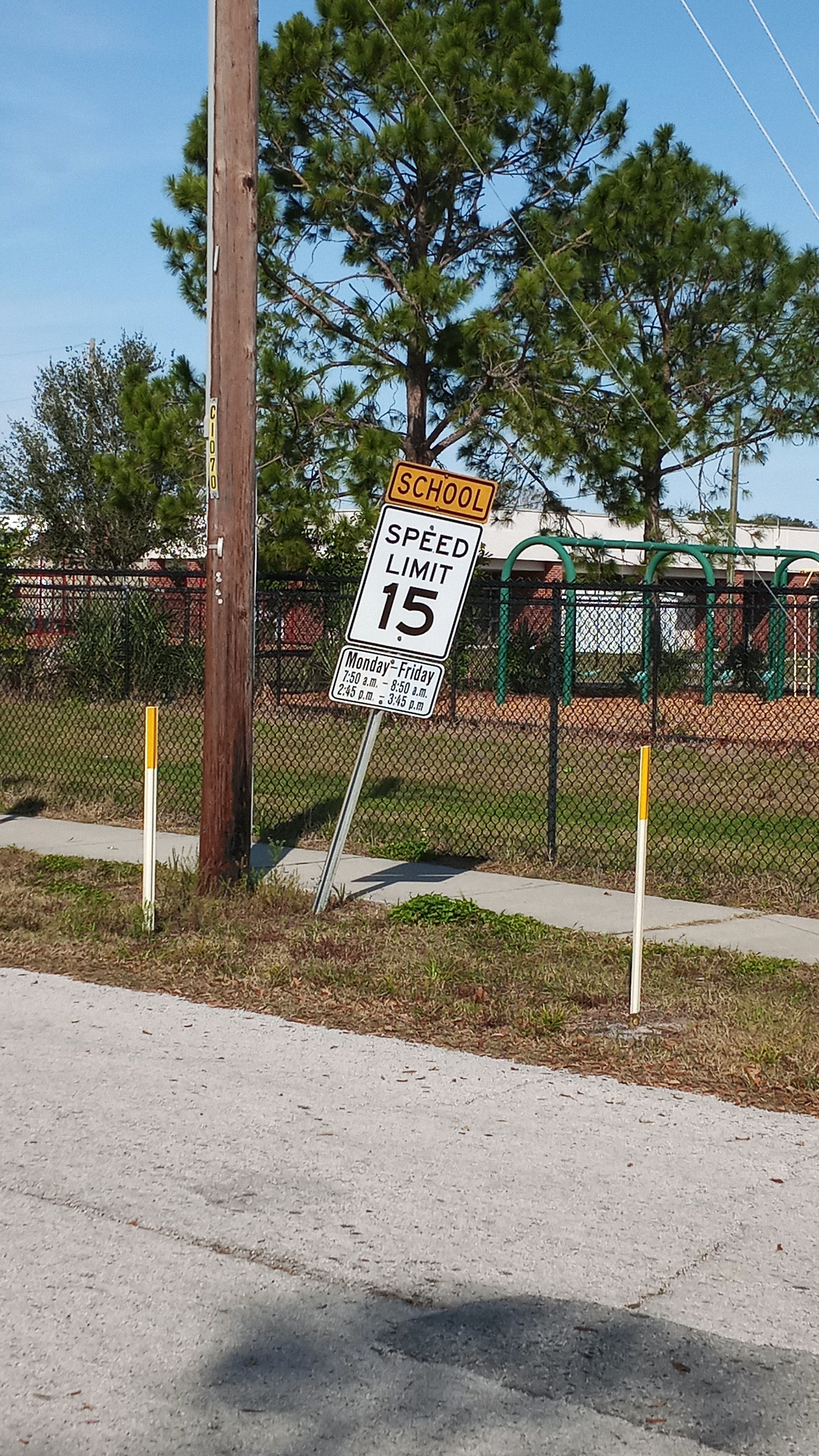 A yellow school zone 15 mph speed limit sign posted near a sidewalk outside a Florida elementary school.