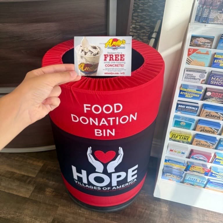 Red and black cylindrical food donation bin labeled HOPE Villages of America indoors.