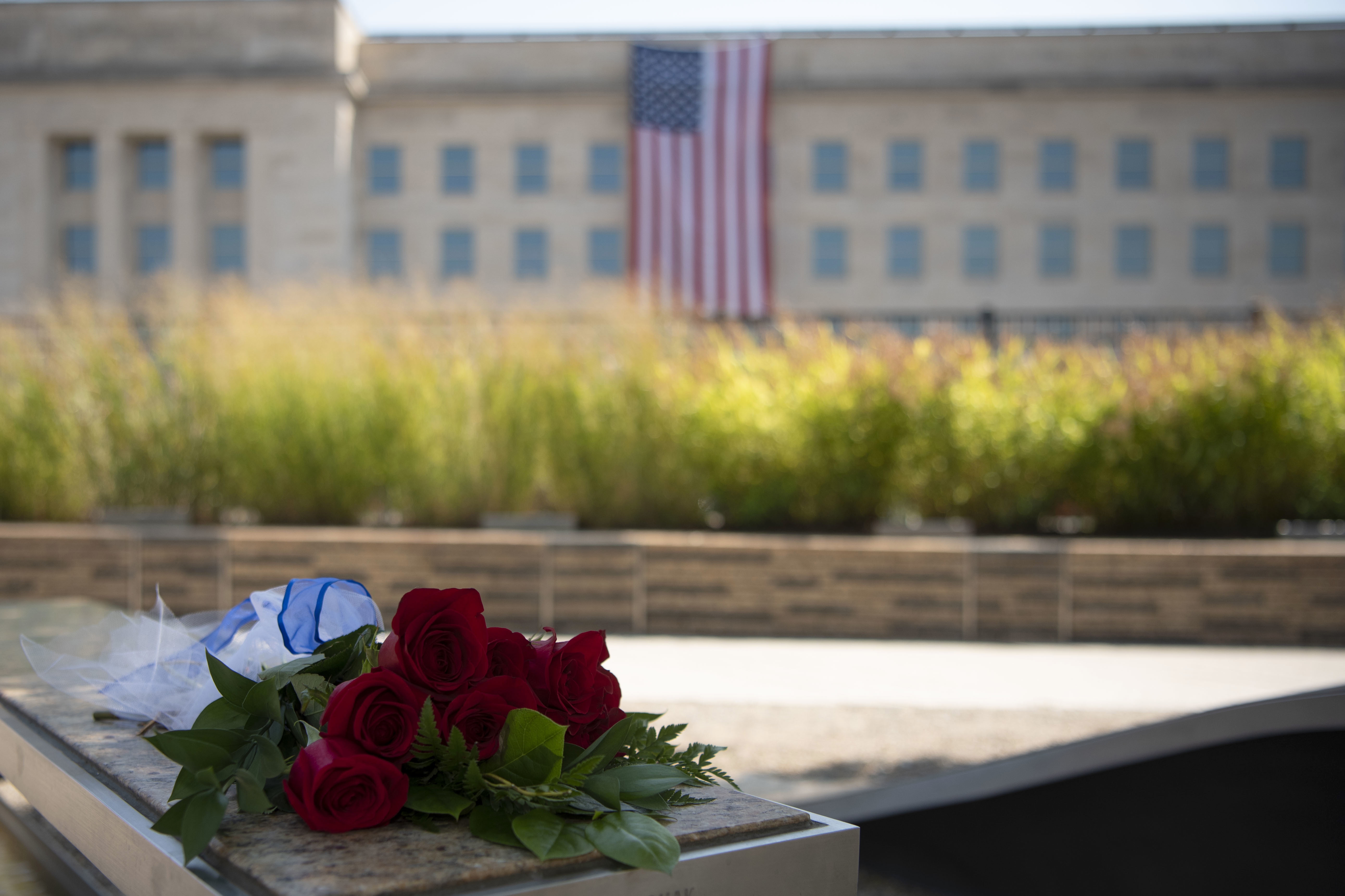 Red roses placed on a memorial bench with the Pentagon and an American flag in the background.