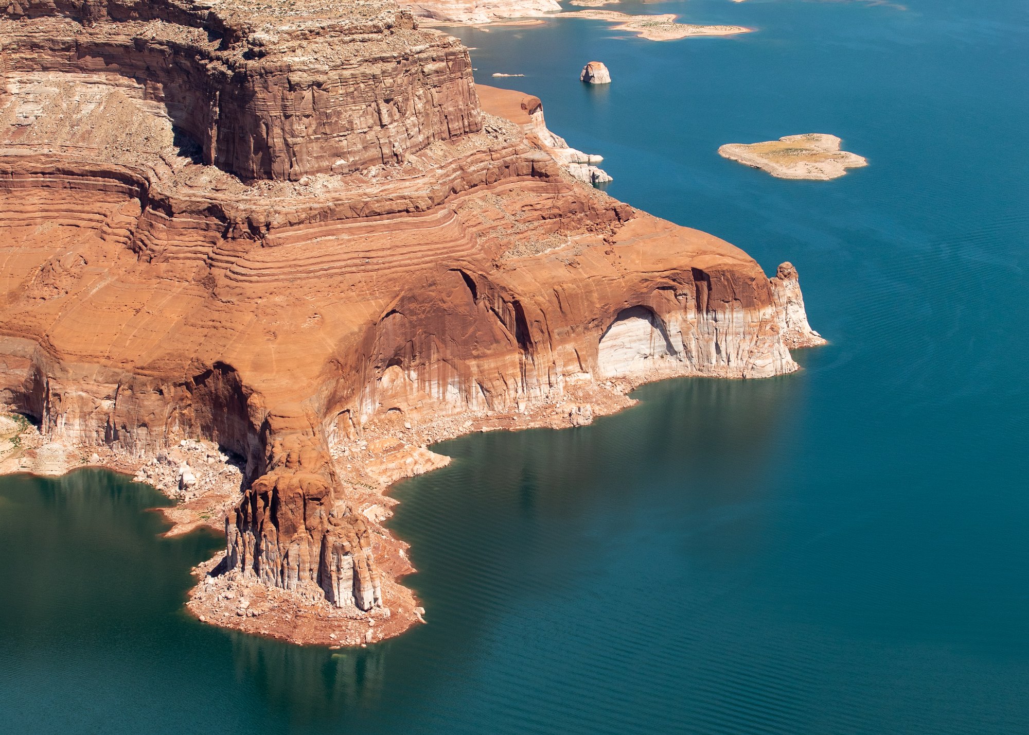 Aerial view of Lake Powell showing exposed red sandstone formations and a white bathtub ring indicating receded water levels.