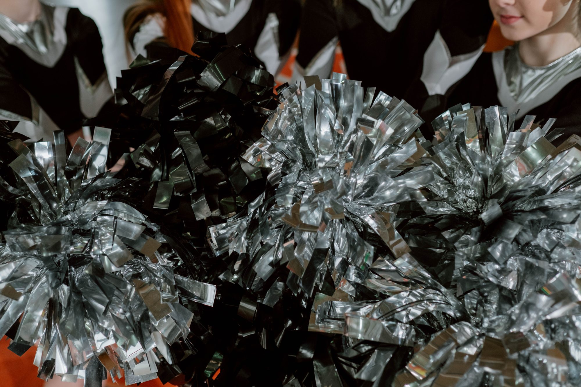 Close-up of cheerleaders with shiny silver pom poms, highlighting team spirit and energy.