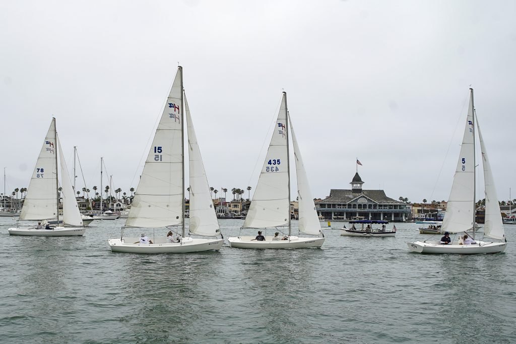 Several small sailboats racing on Newport Harbor with the Balboa Pavilion in the background.