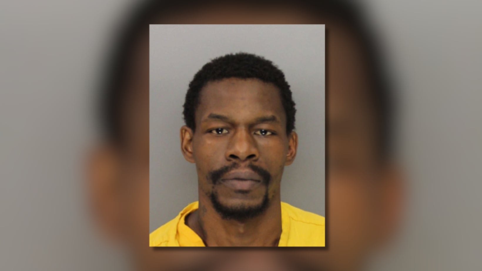 Man in yellow jail garment photographed against a gray background in a booking photo.