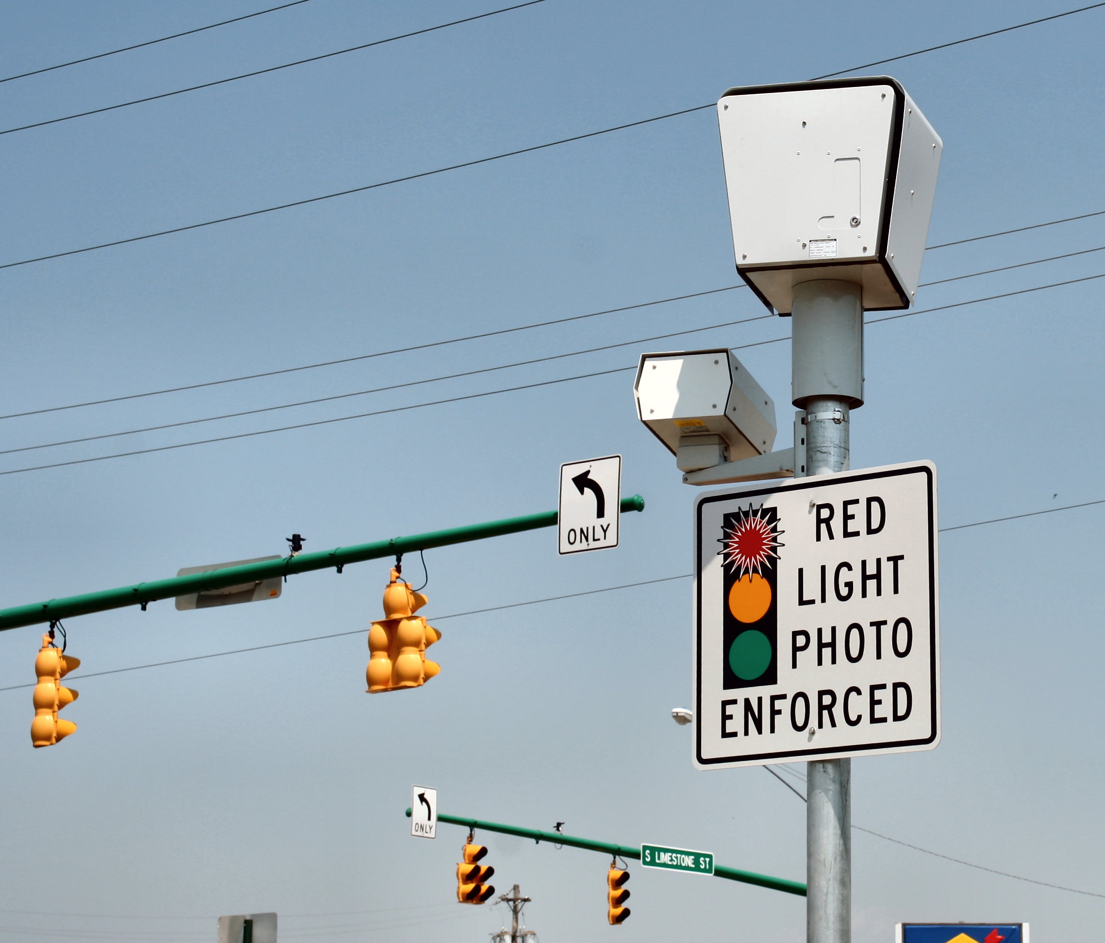 Red-light enforcement camera and warning sign mounted on a pole above an intersection.