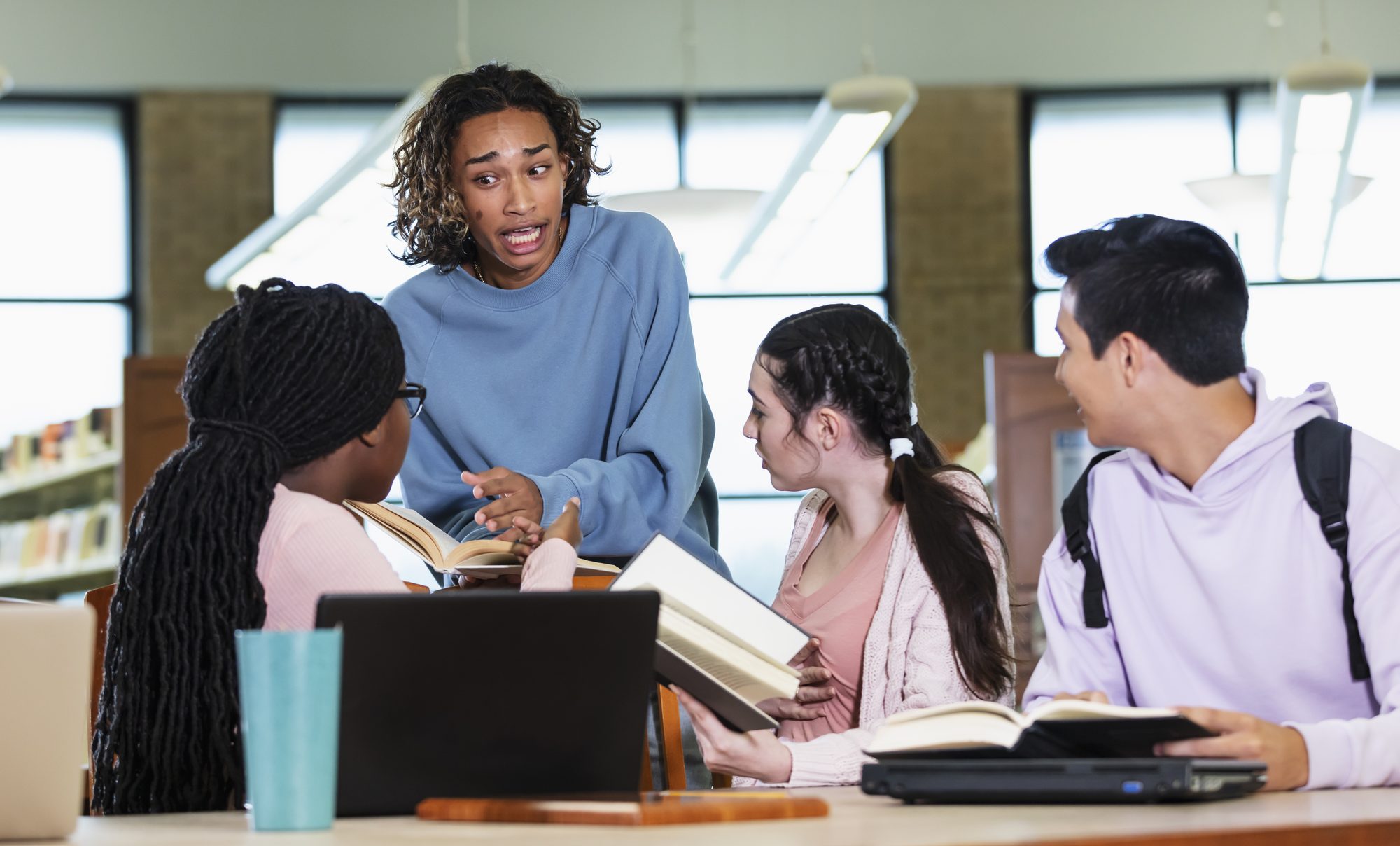 Four multiracial high school students talking in library