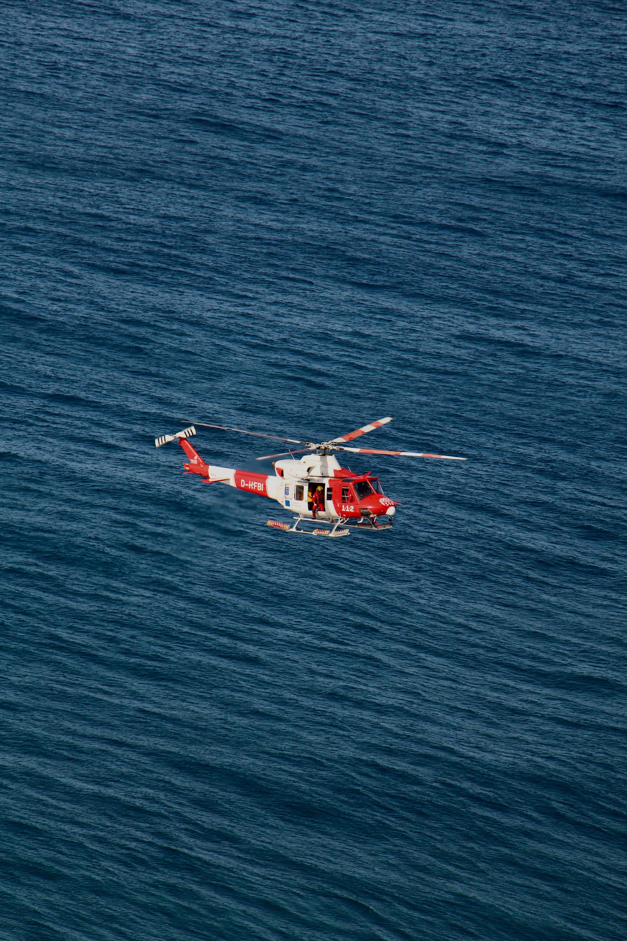 Aerial view of a red rescue helicopter flying above deep blue ocean waters.