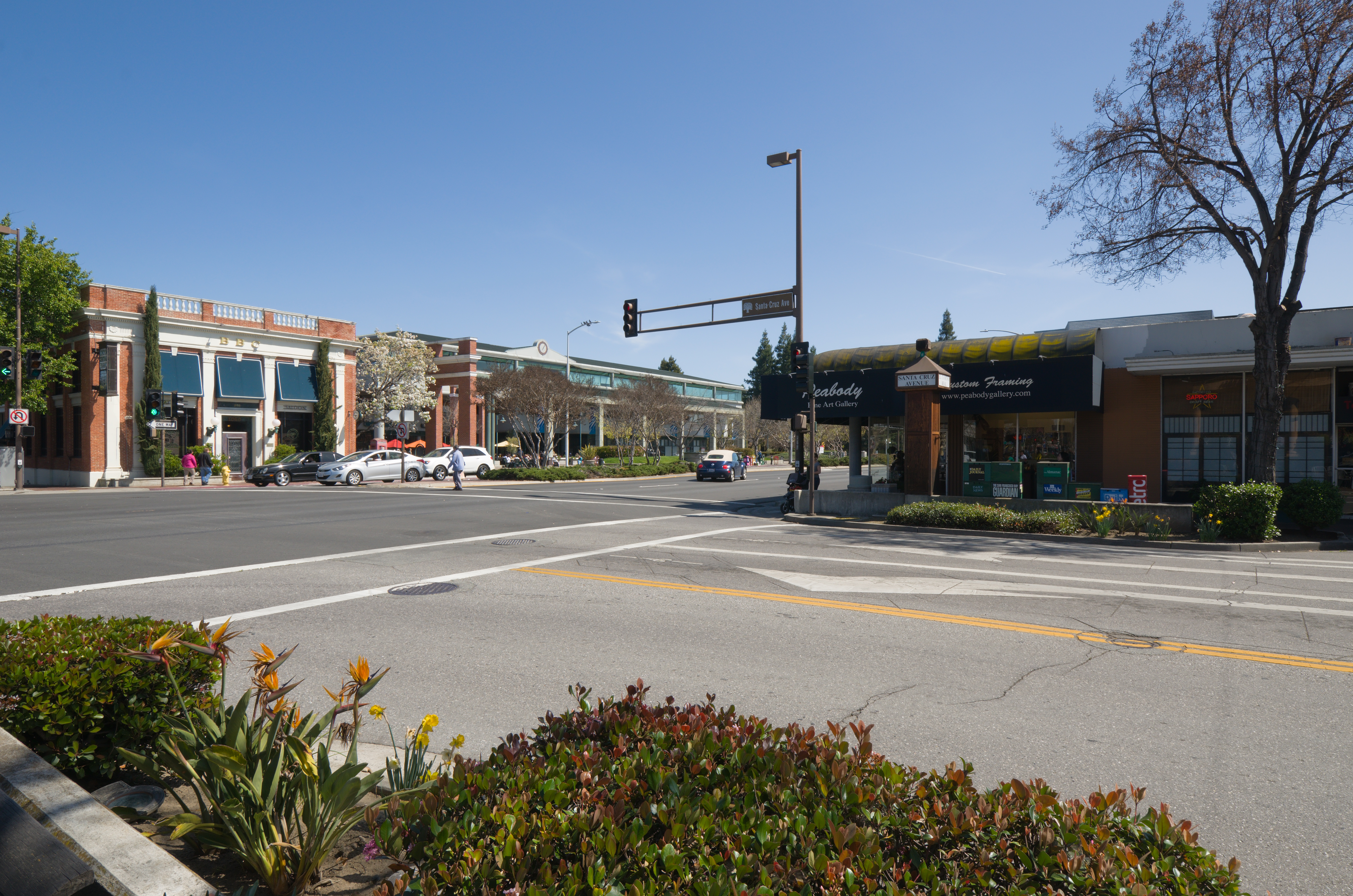 Downtown Menlo Park street with storefronts, traffic signal, and surface parking area.