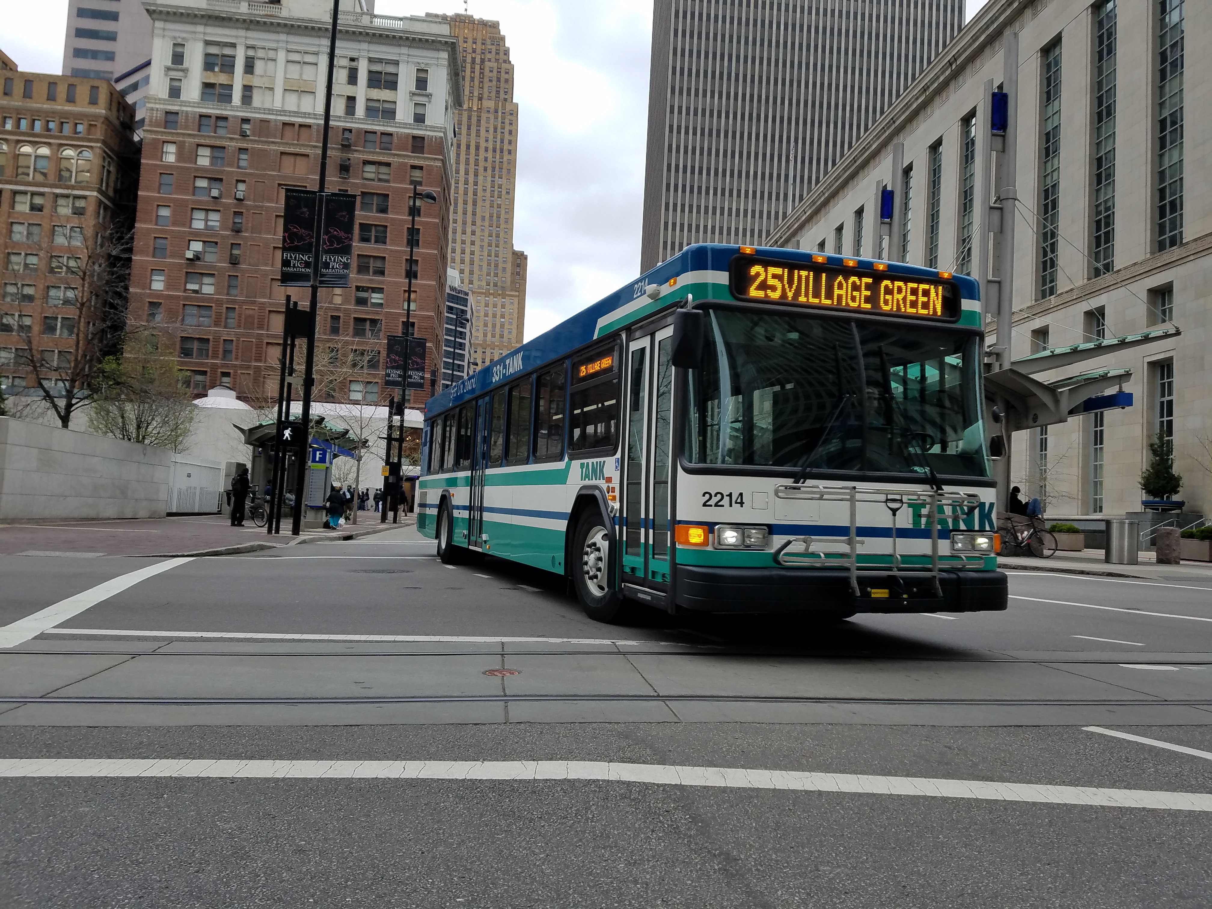 A teal and white TANK bus displaying Route 25 turns at a downtown Cincinnati intersection.