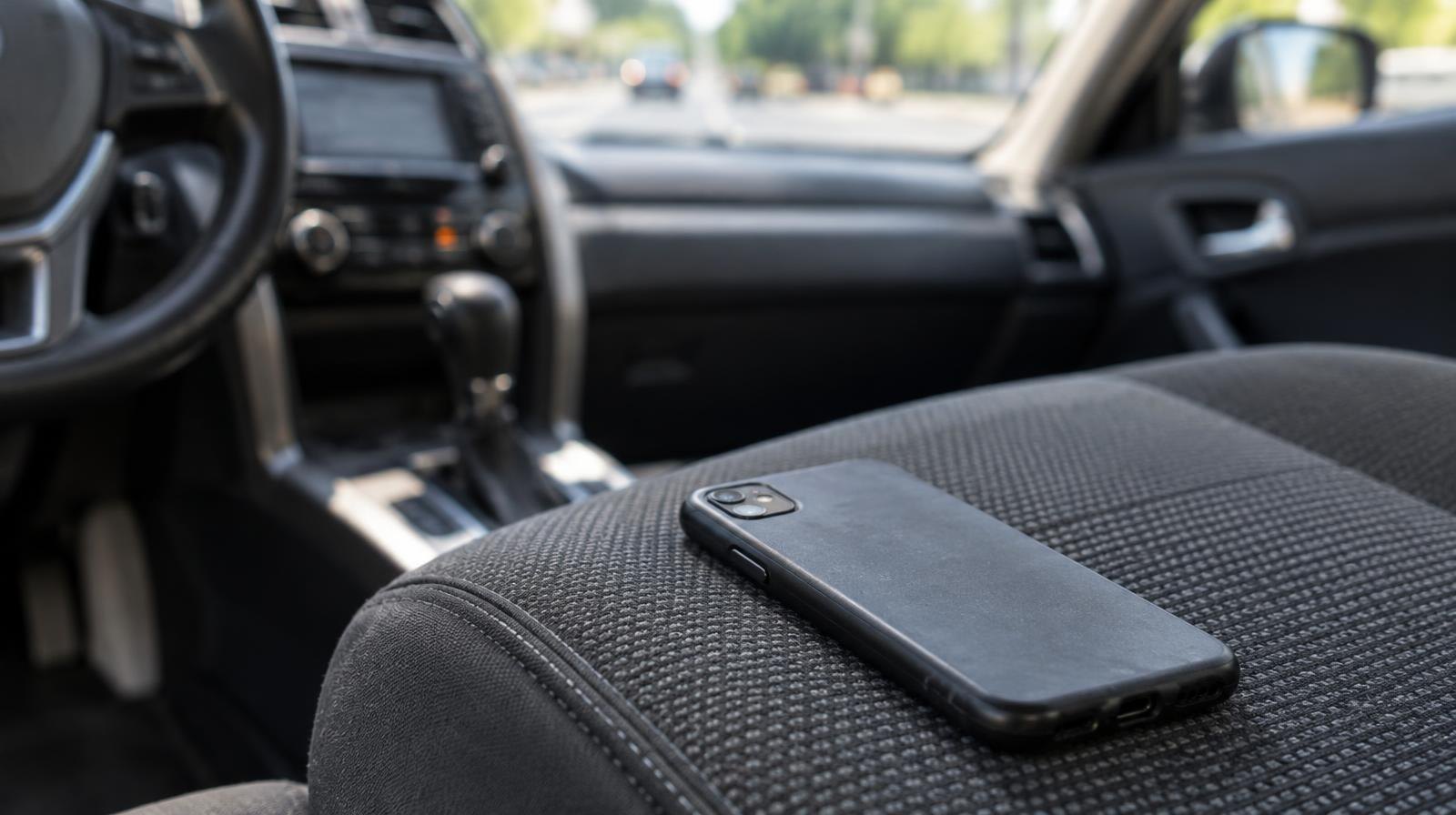 A smartphone placed face-down on a car seat with a road visible through the windshield.