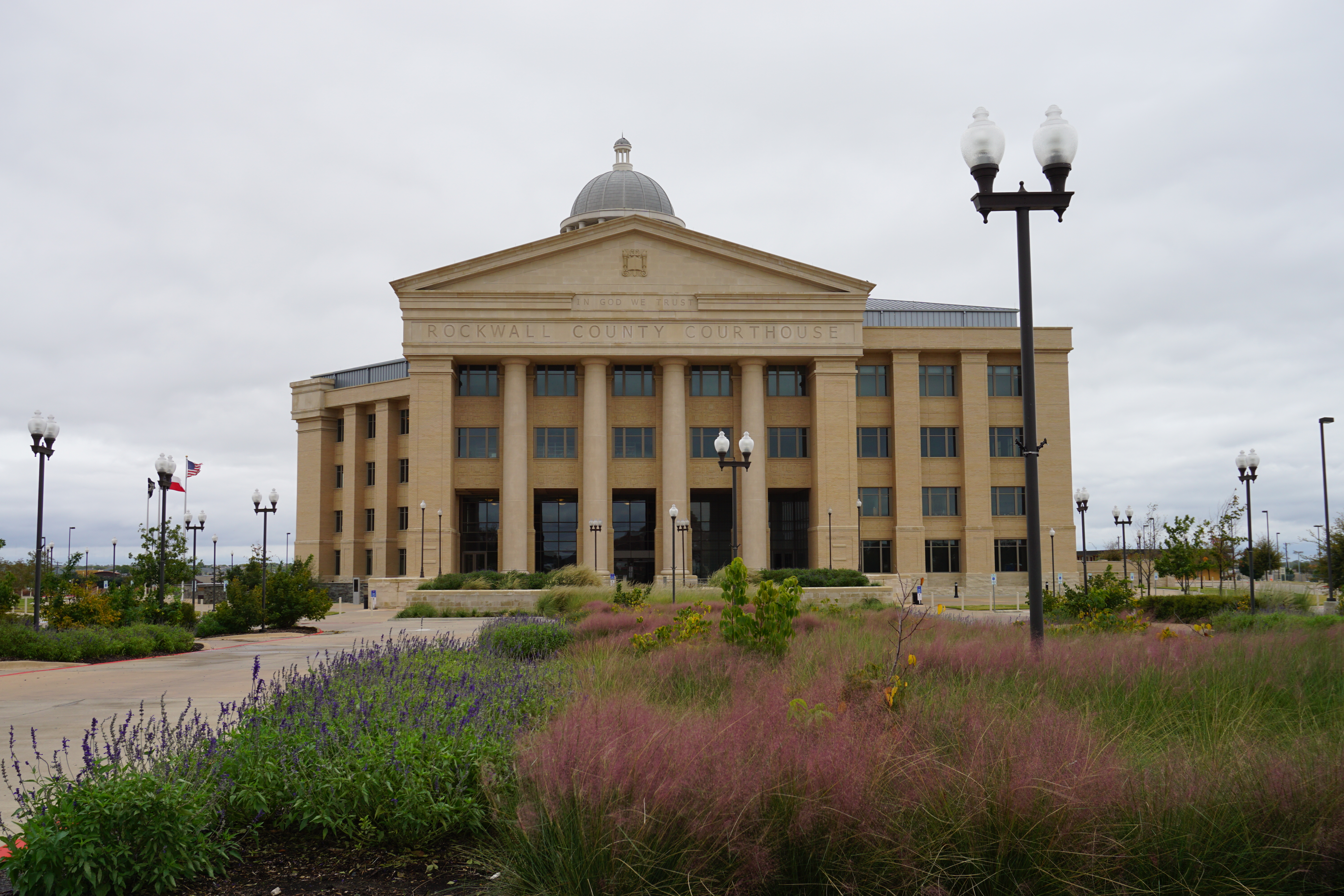 Neoclassical courthouse with dome, columns, American flags, and colorful wildflowers in front.