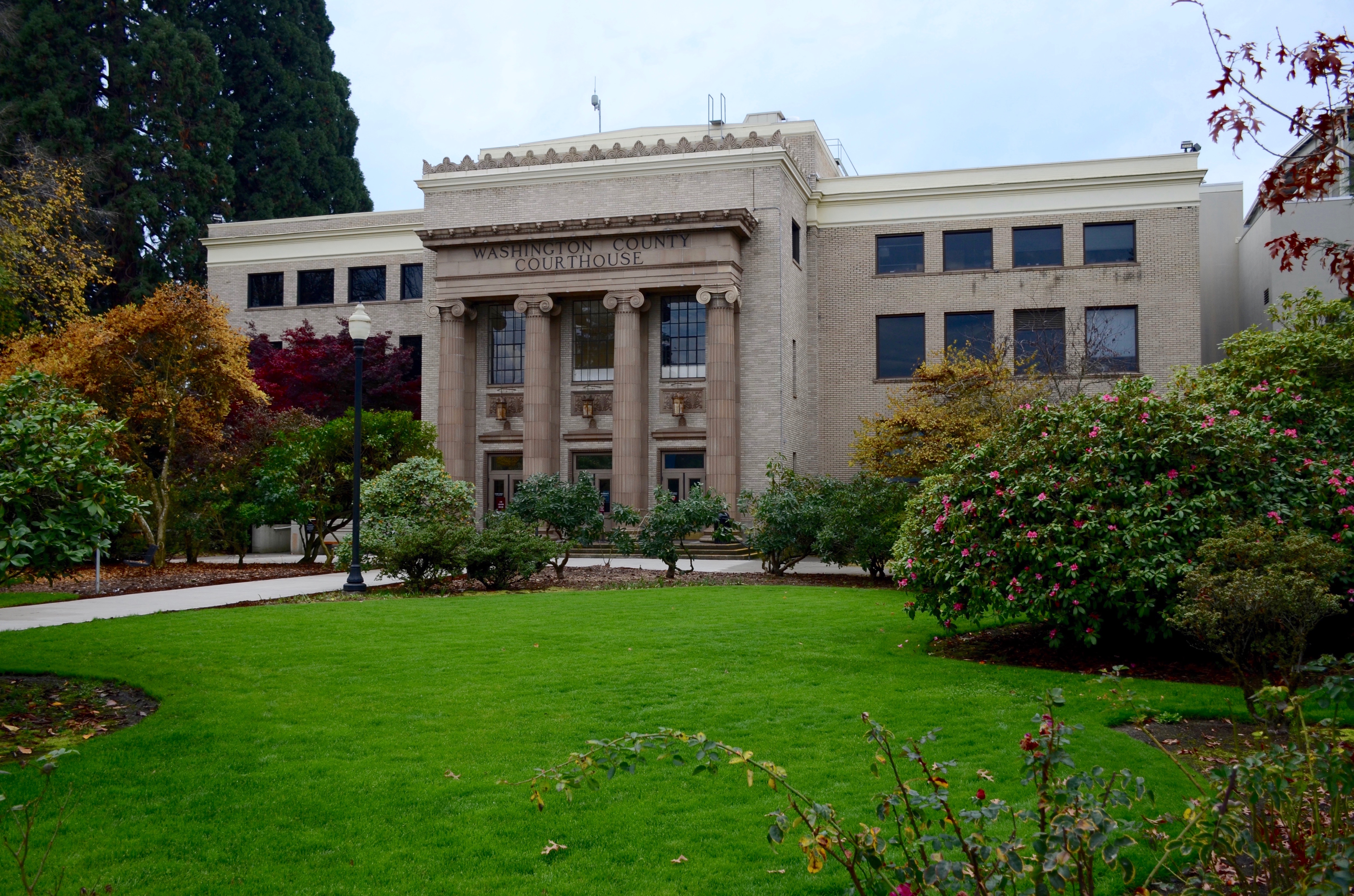 Neoclassical stone courthouse with columns, surrounded by green lawn and autumn-colored trees.