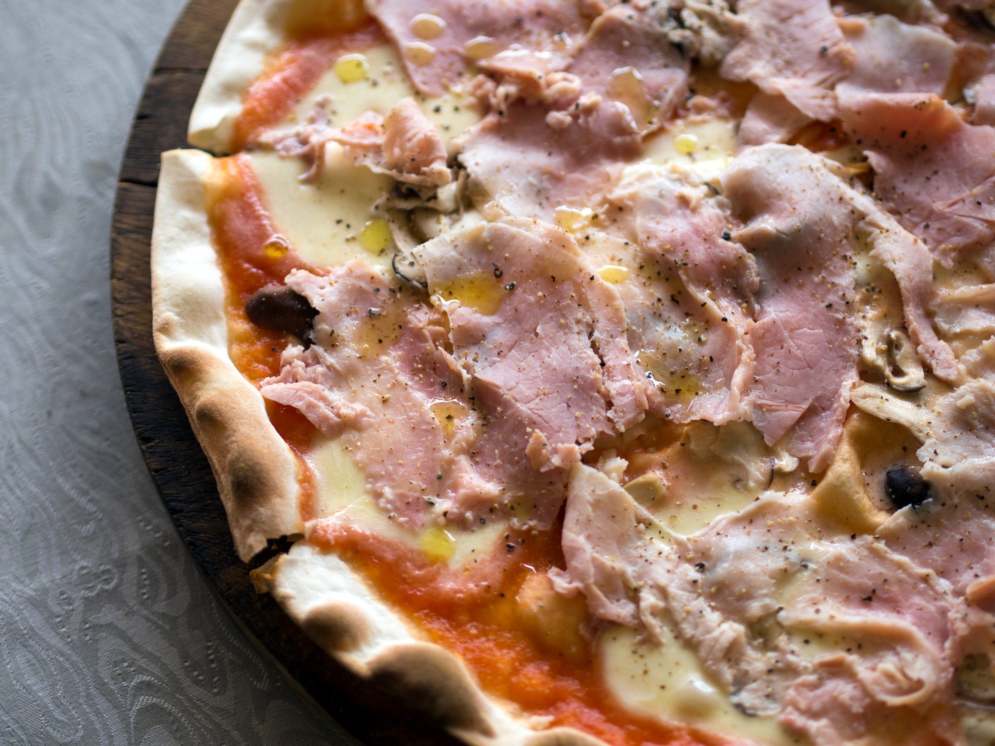 Pizza regina, pizza con funghi e prosciutto cotto e mozzarella di bufala: pizza with mushroom, cooked ham, and buffalo mozzarella, at an Italian restaurant in Chiang Mai, Thailand. The ultra thin crust is conform the Roman style of pizza. The buffalo mozzarella is a local produce of Thailand. Olive oil and pepper were added when it arrived at the table.