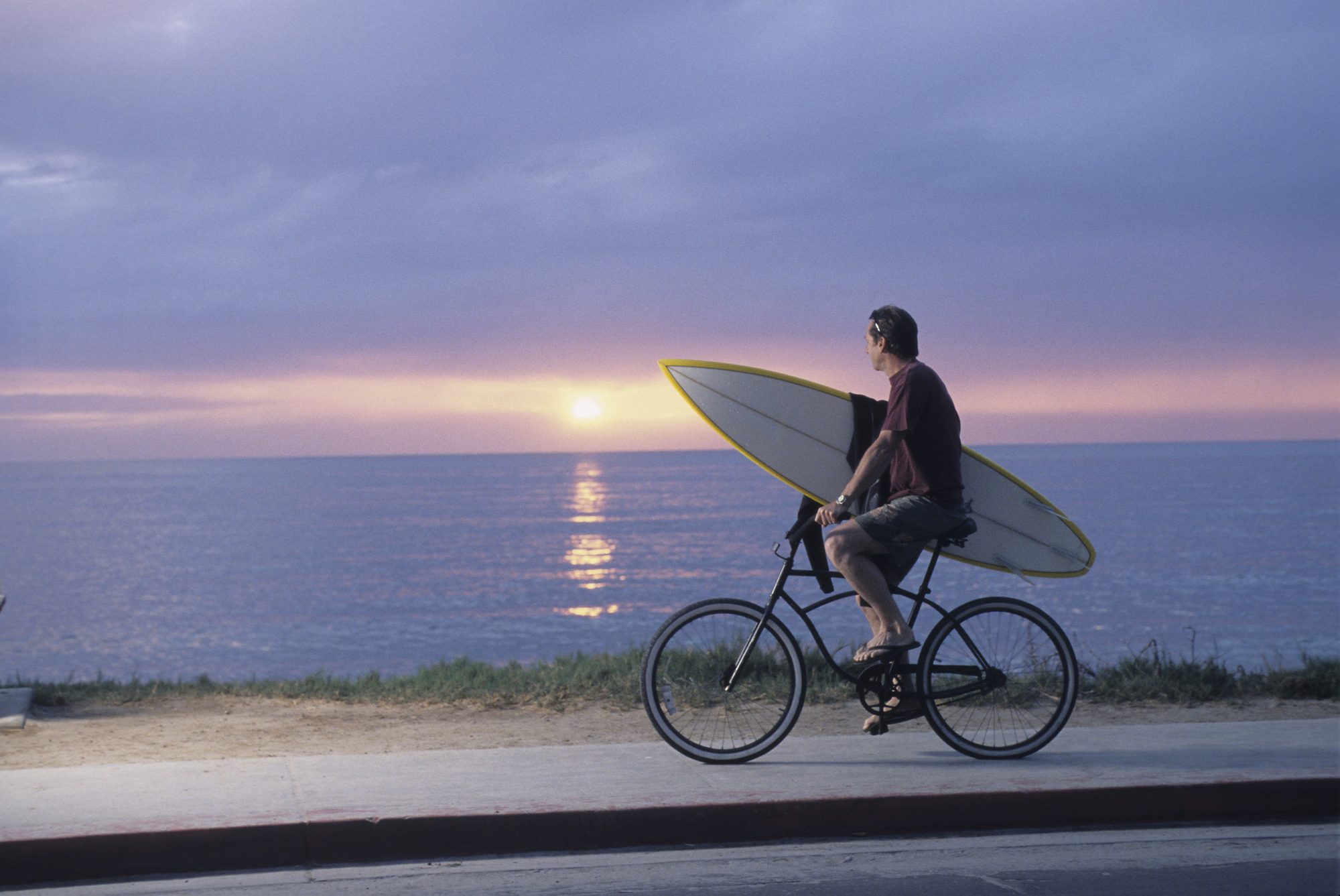 Man riding bike with surfboard in La Jolla, California.