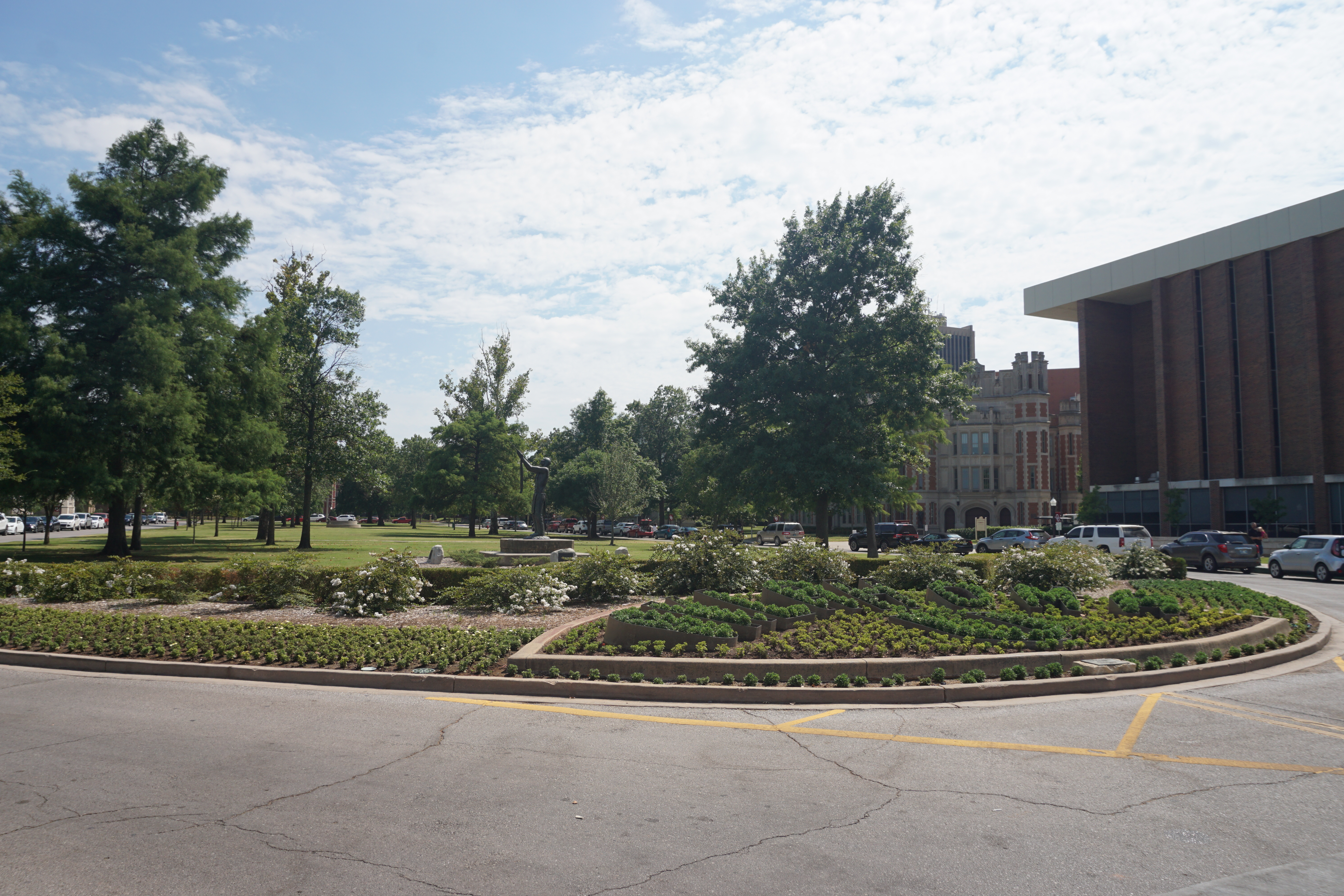 Landscaped oval plaza with curved garden beds and mature trees on a university campus.