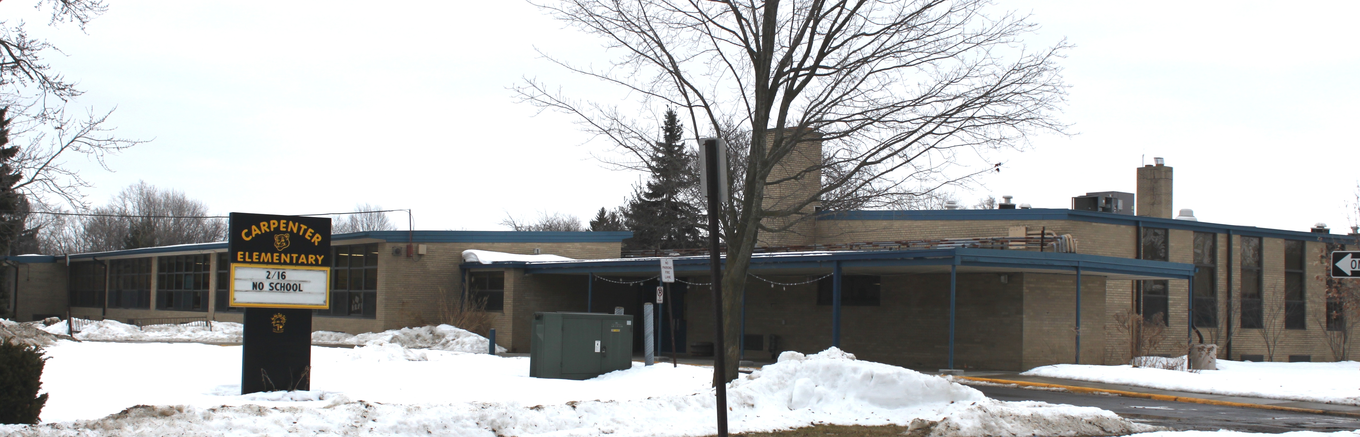 Single-story brick school building with a marquee sign in a snowy winter setting.