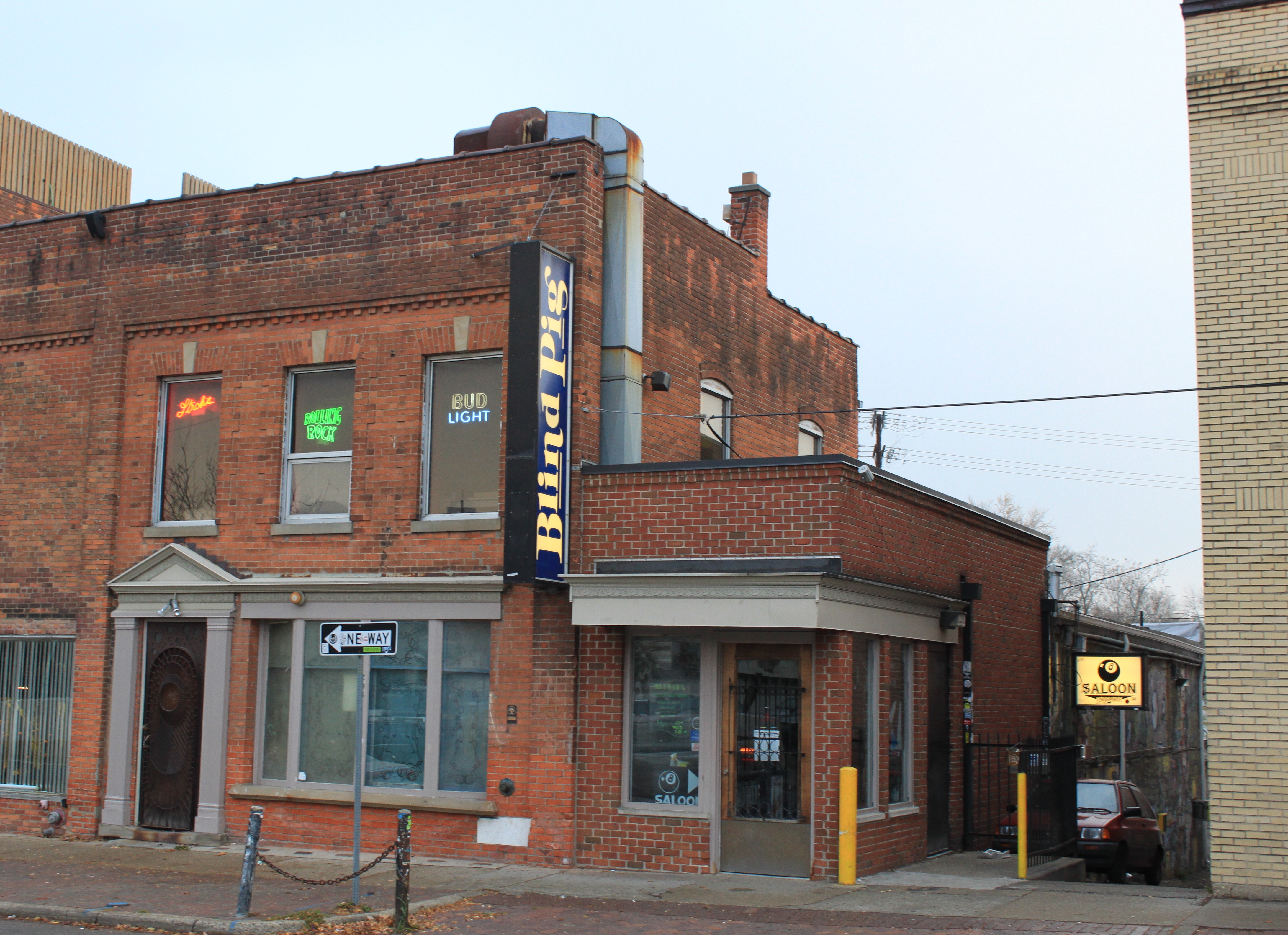 Two-story brick corner building with a vertical Blind Pig banner sign.