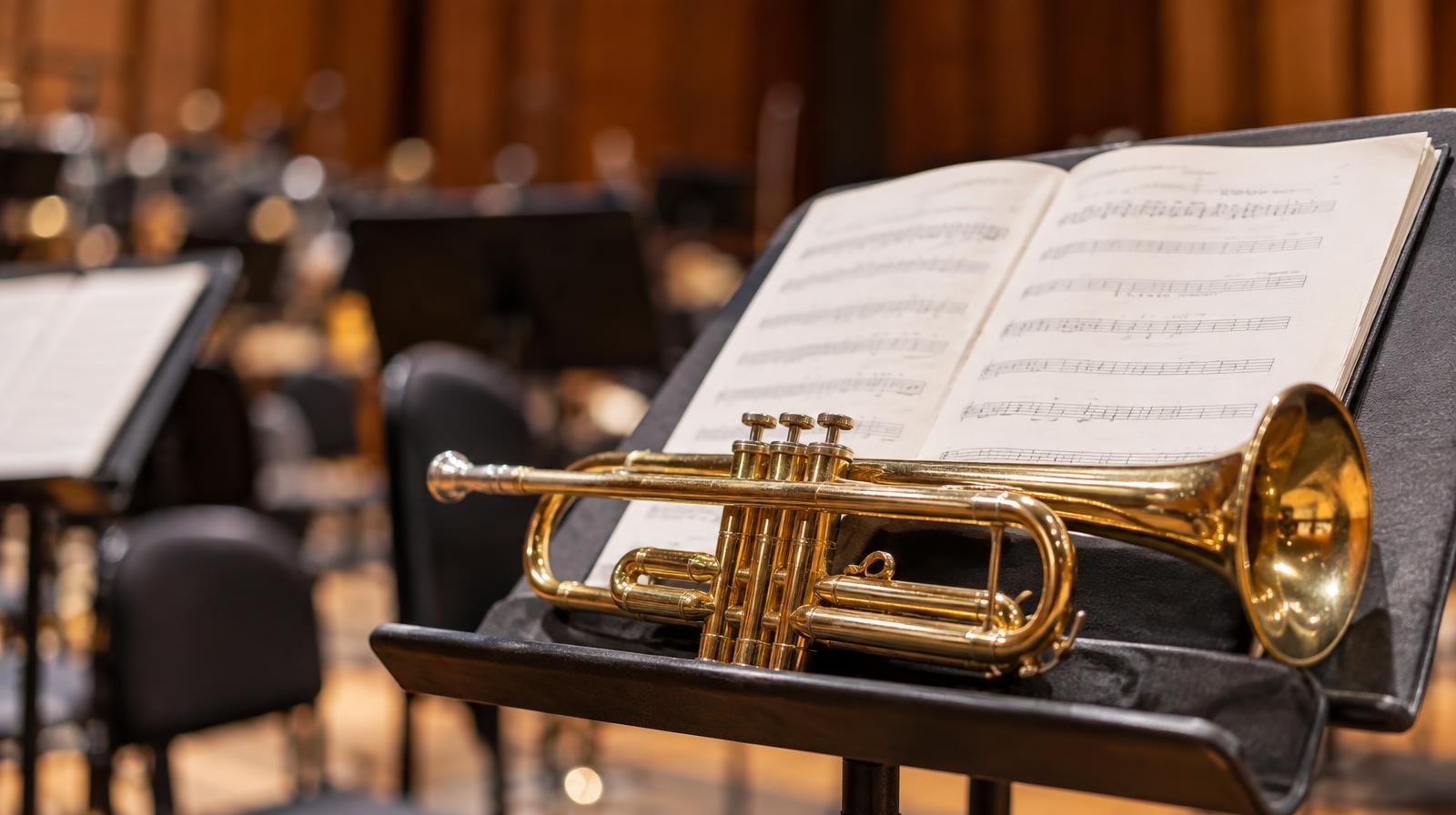 A polished brass trumpet resting on a music stand with sheet music under warm lighting.