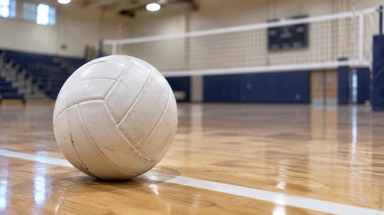 White volleyball on a hardwood gym floor beside a volleyball net.