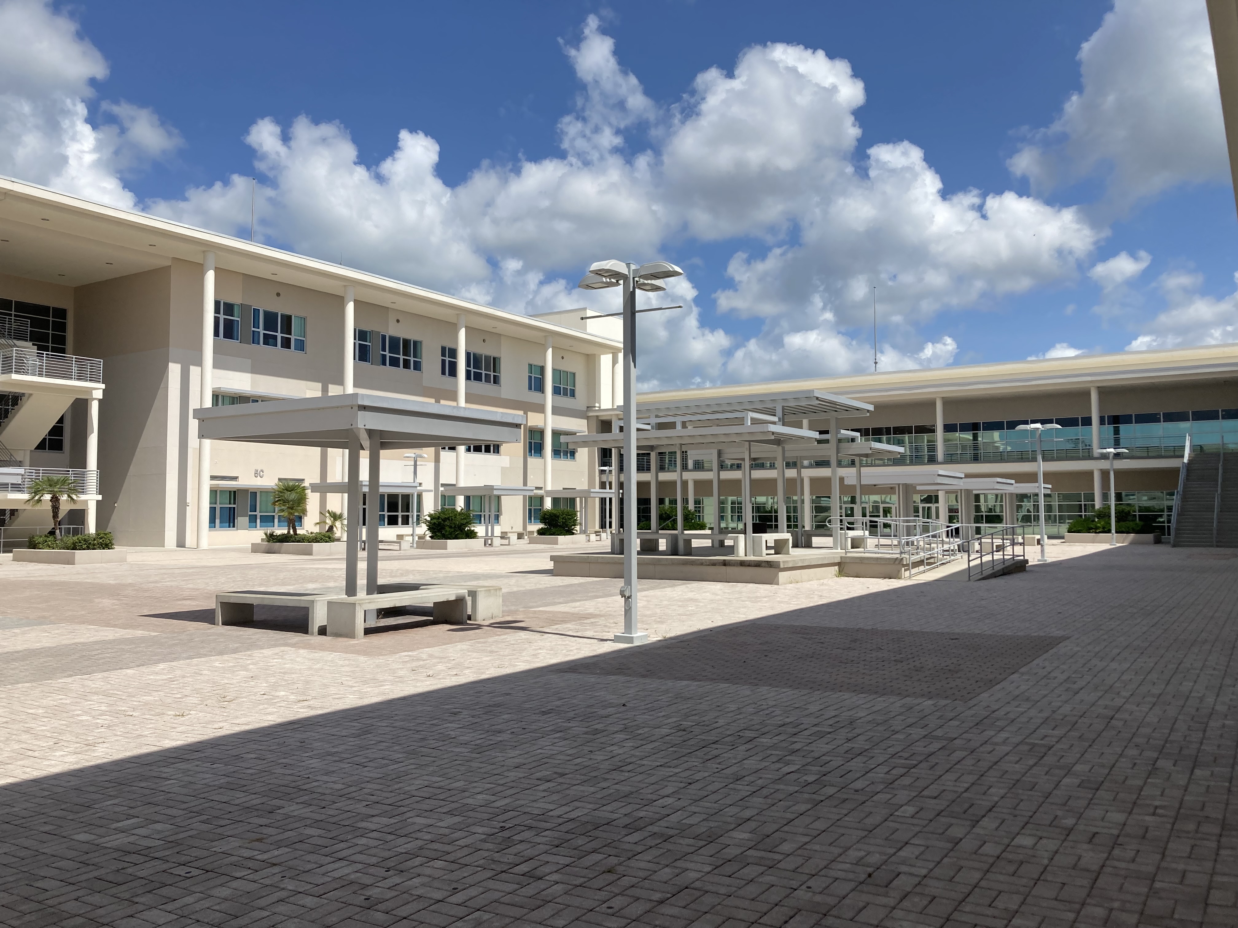 Open courtyard at a modern two-story high school with shade canopies and brick pavers.