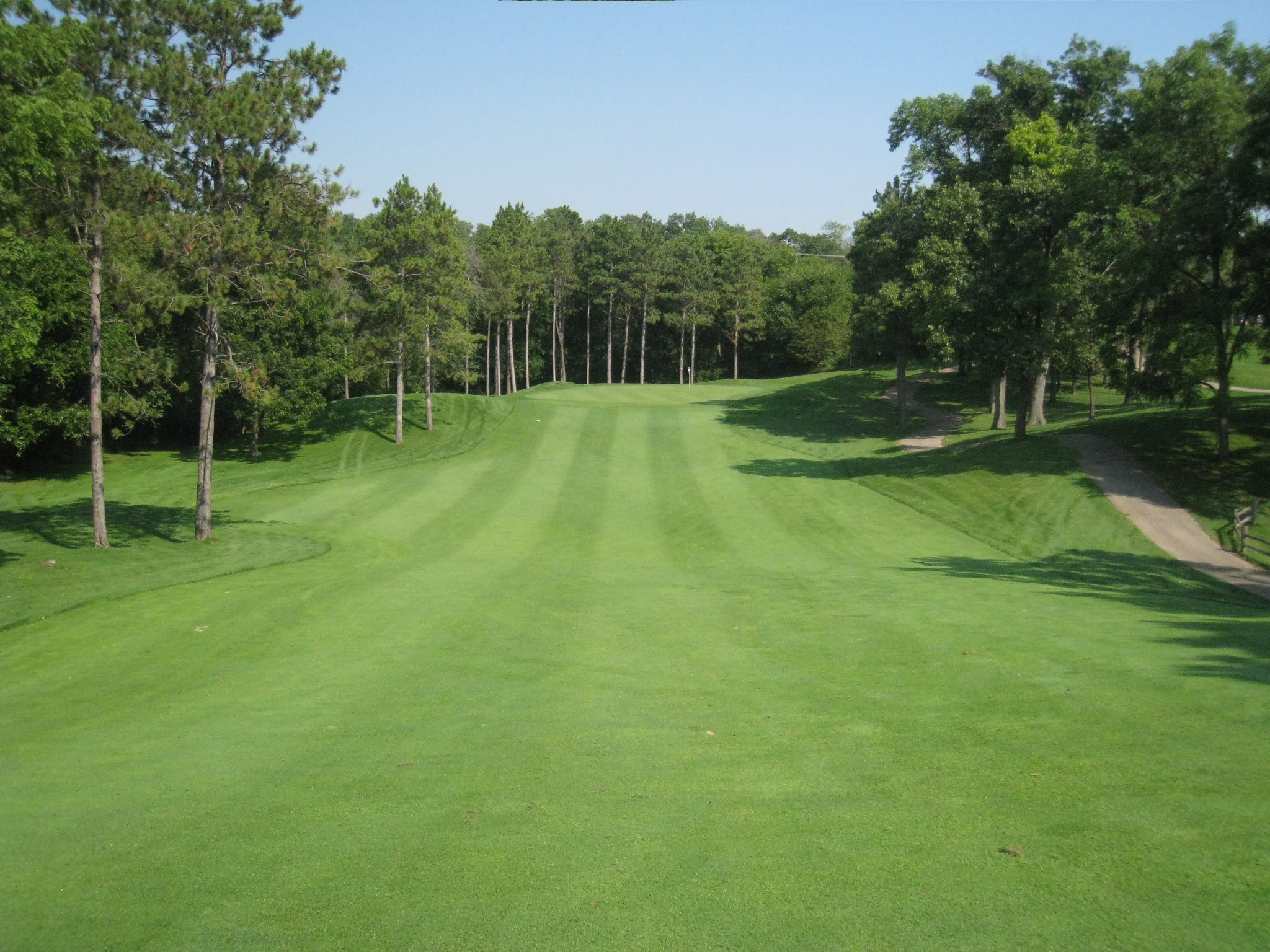 A lush golf course fairway lined with trees under a clear blue sky.