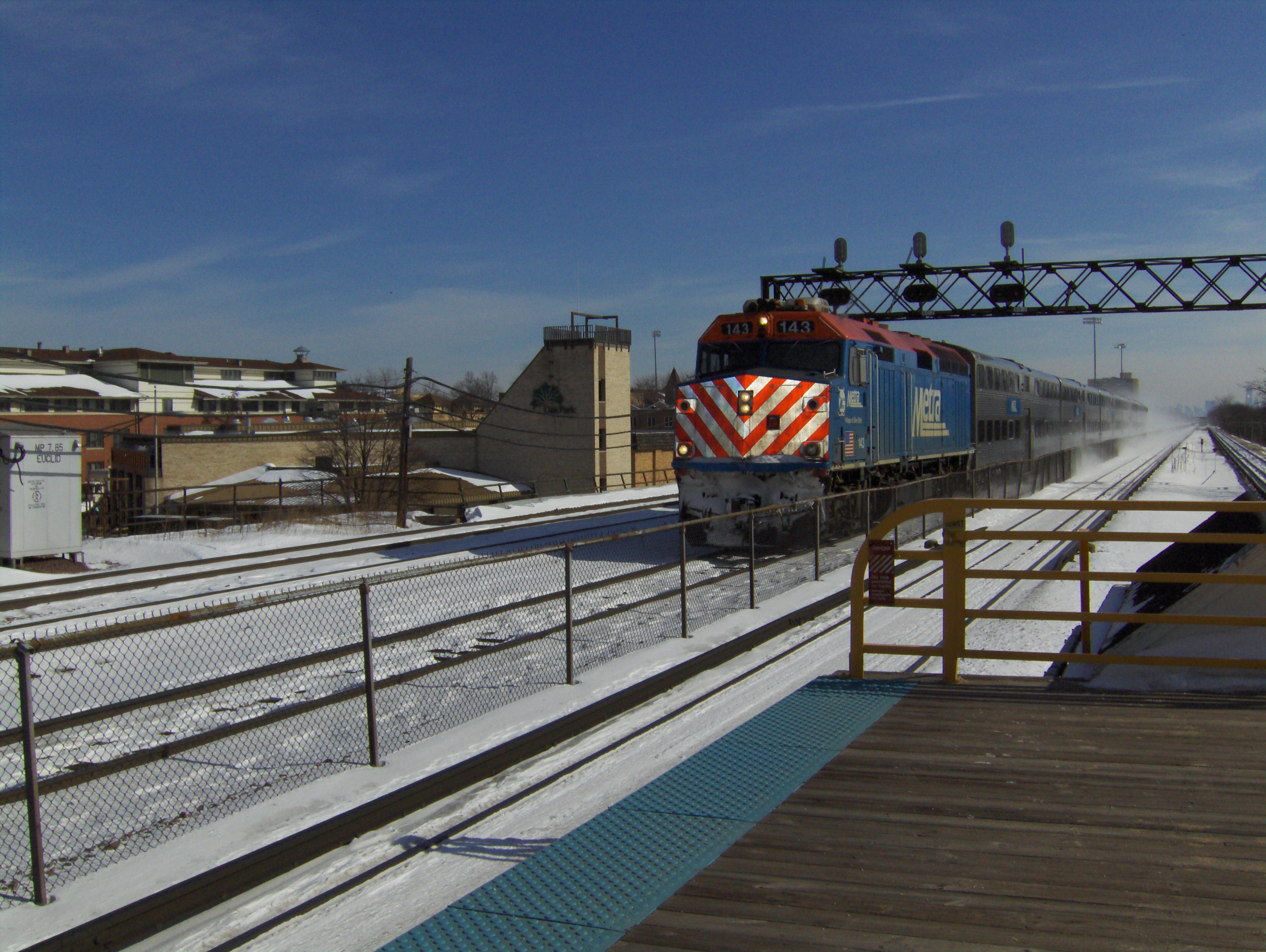 A blue and white Metra UP-W locomotive approaches on snow-covered tracks.