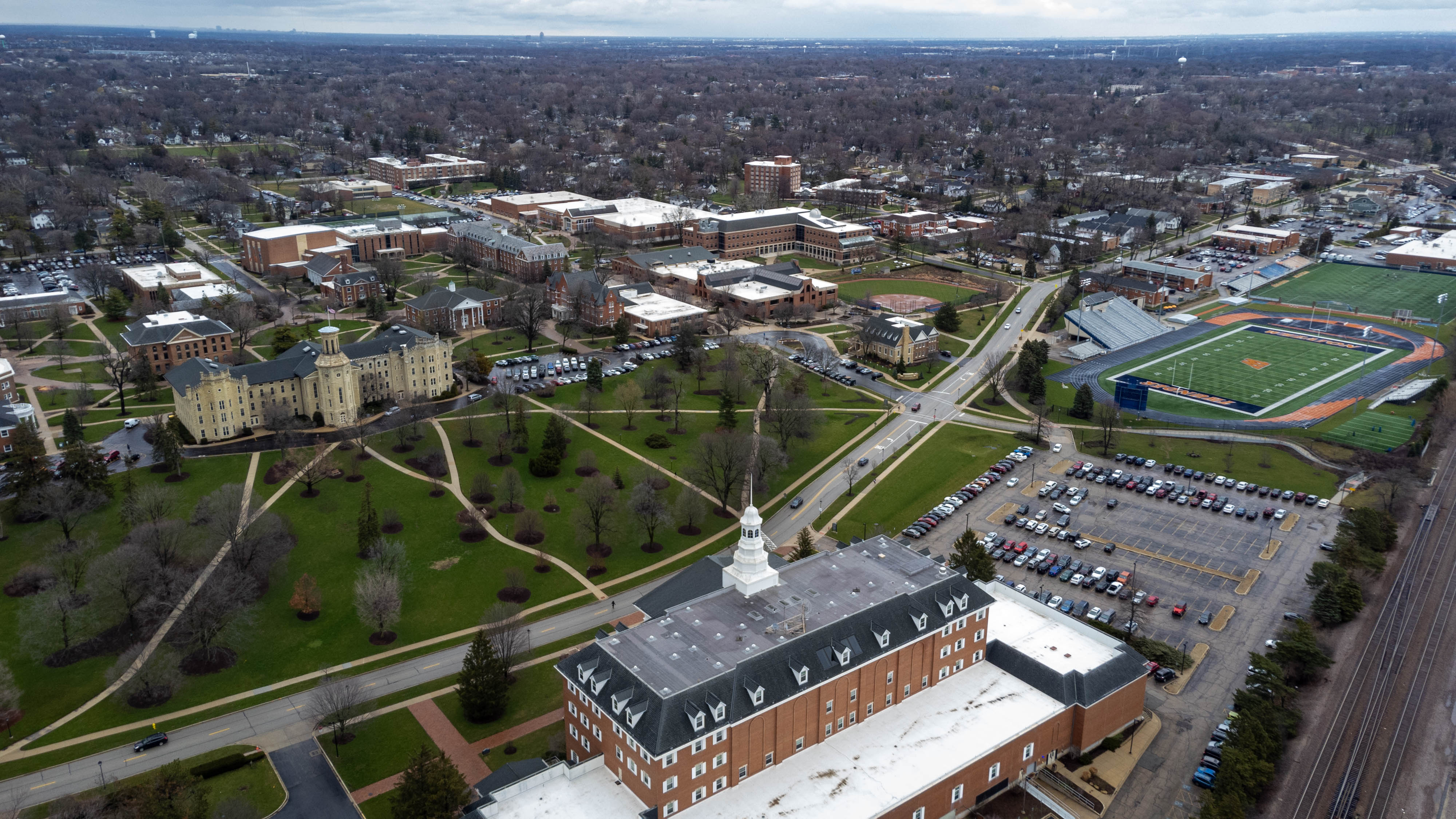 Aerial view of a college campus with brick buildings, green lawns, and athletic fields.