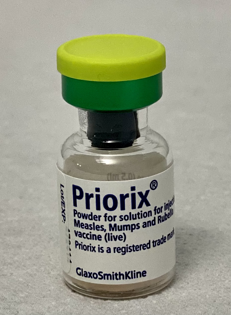 Small glass vial of MMR vaccine with a yellow-green cap on a gray surface.