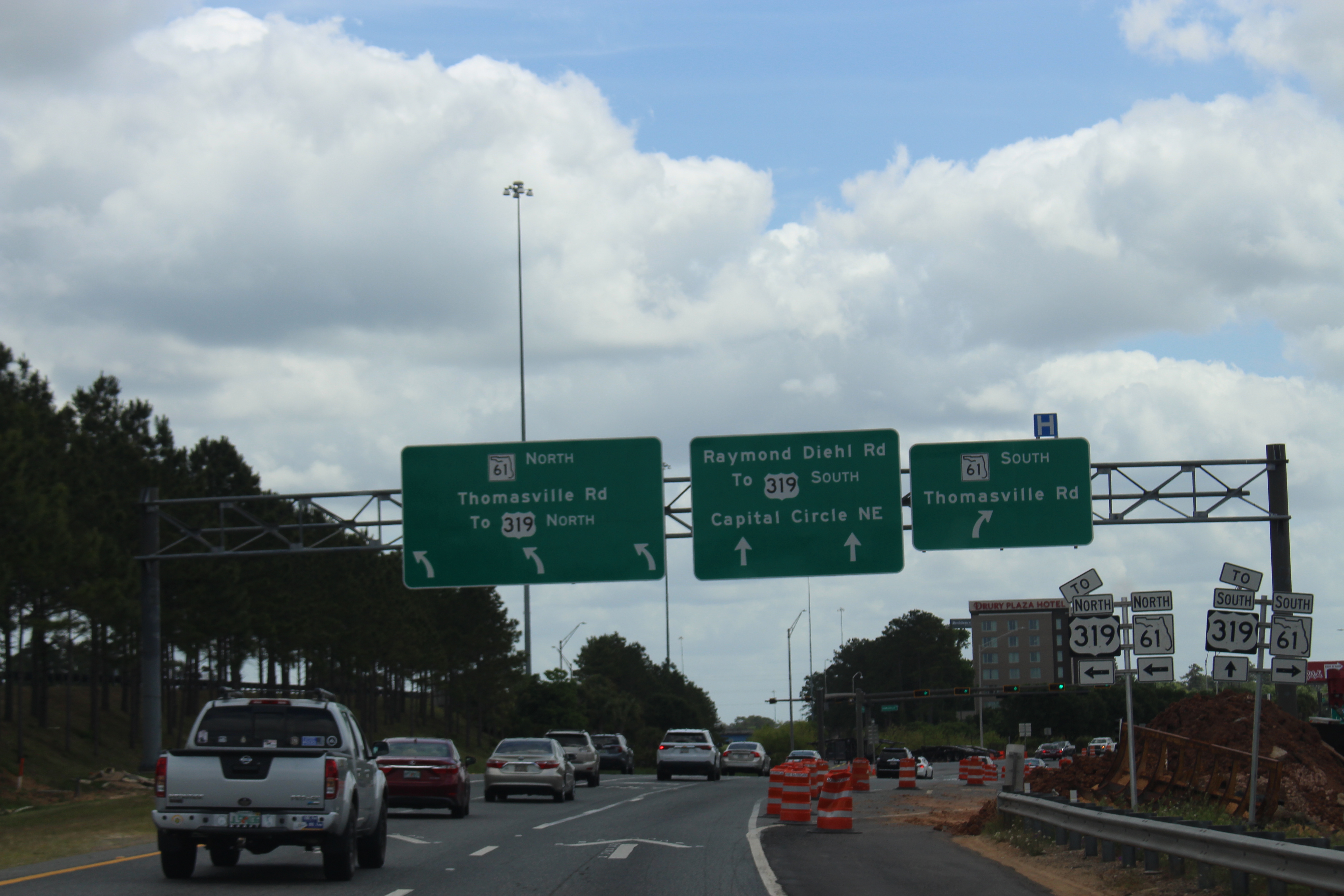 Multi-lane highway with green overhead gantry signs and orange construction barrels ahead.