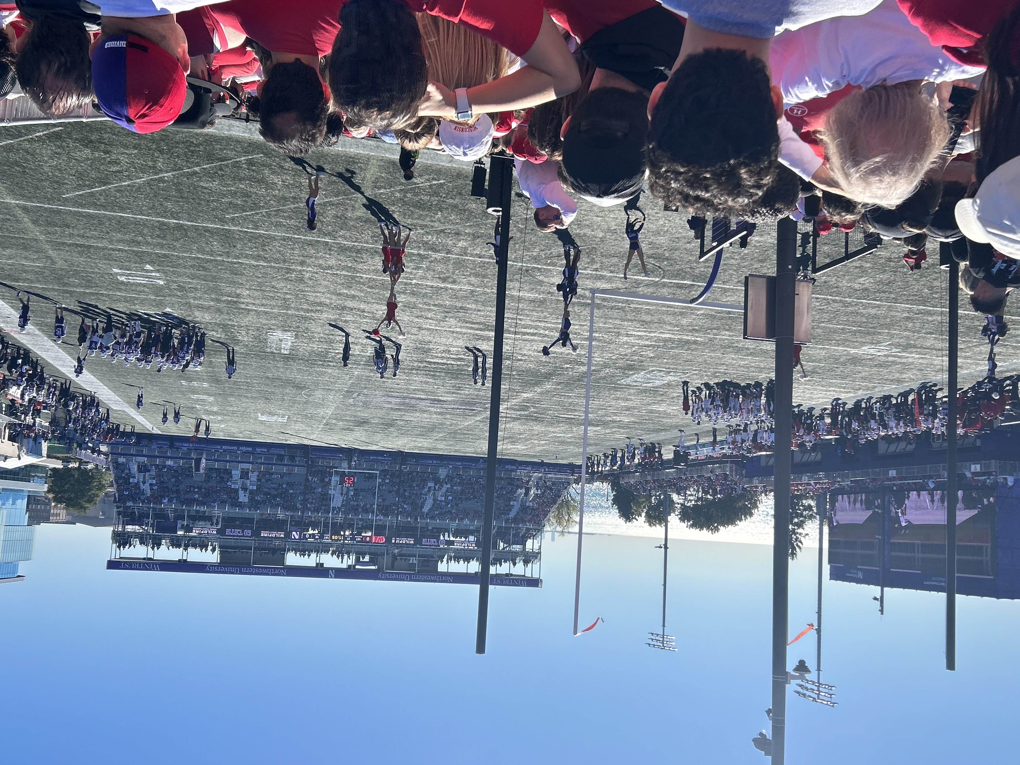 Football stadium with cheerleaders on the field and fans filling the sunny stands.