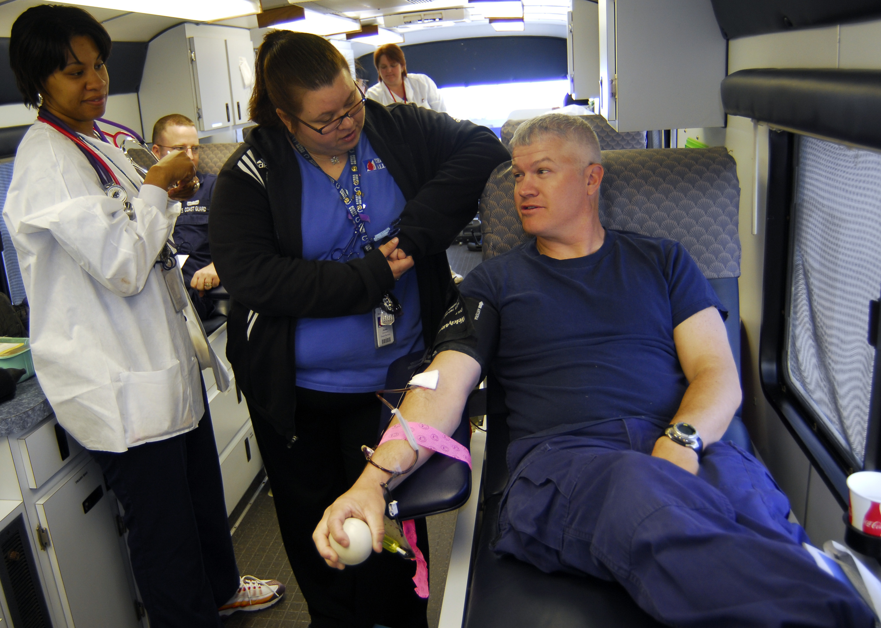 A man donates blood while a technician assists inside a mobile donation unit.