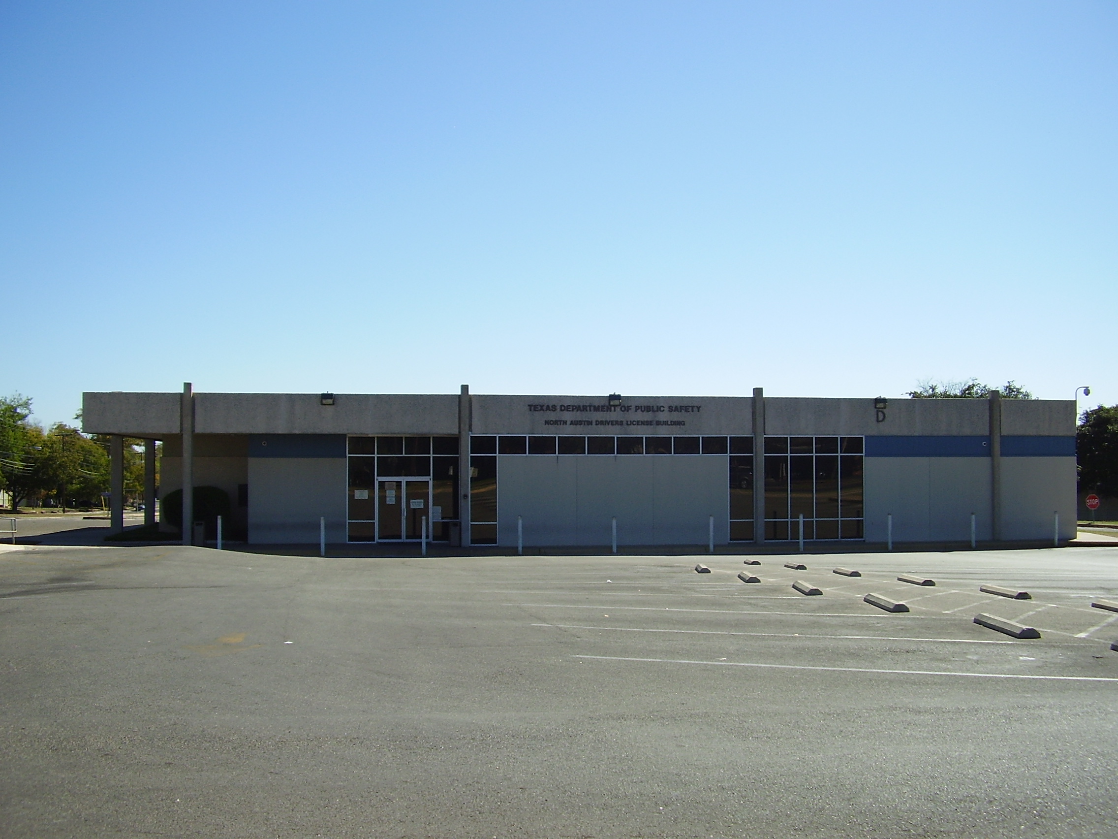 Single-story government building with blue accent stripes and a large empty parking lot.