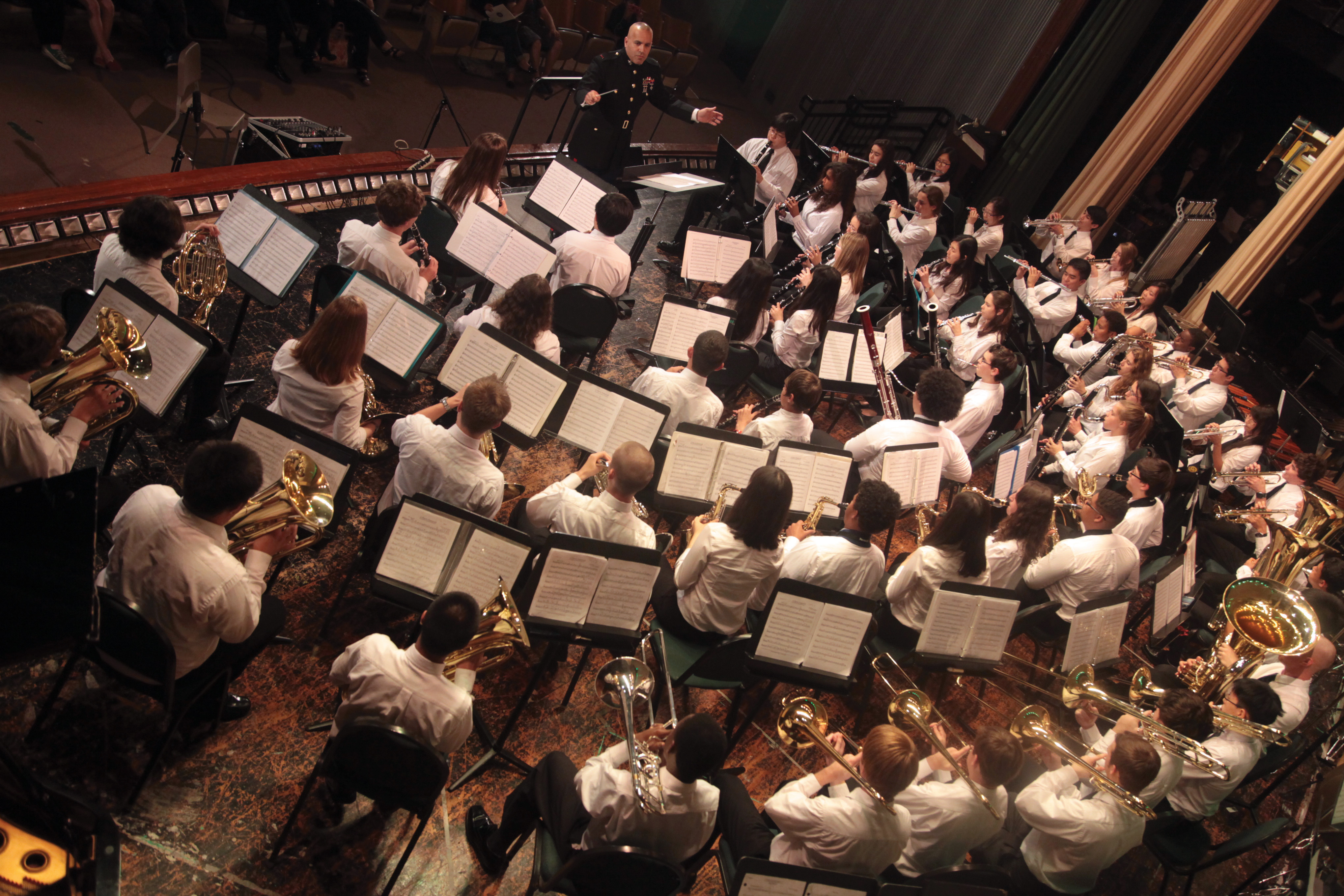 Overhead view of a large concert band seated at music stands in a concert hall.