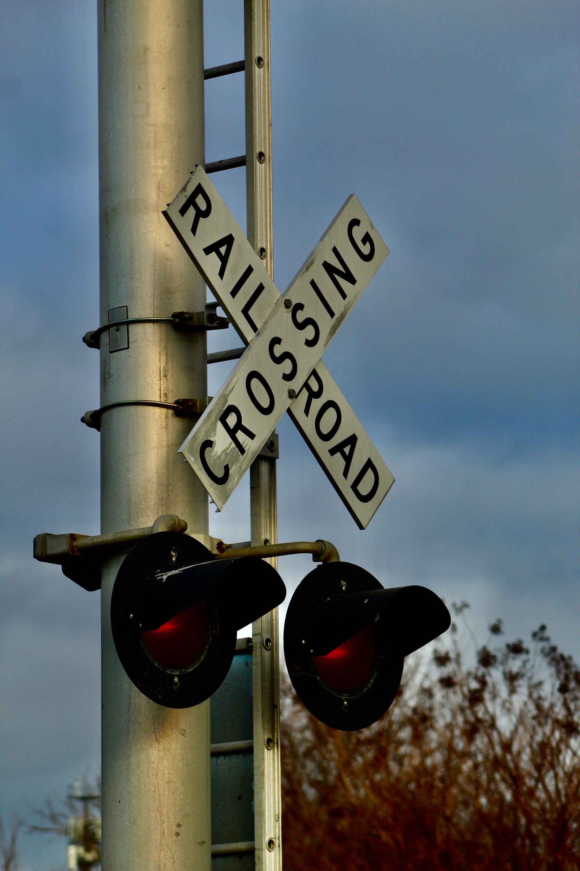 Railroad crossing sign with illuminated red lights against a cloudy sky.