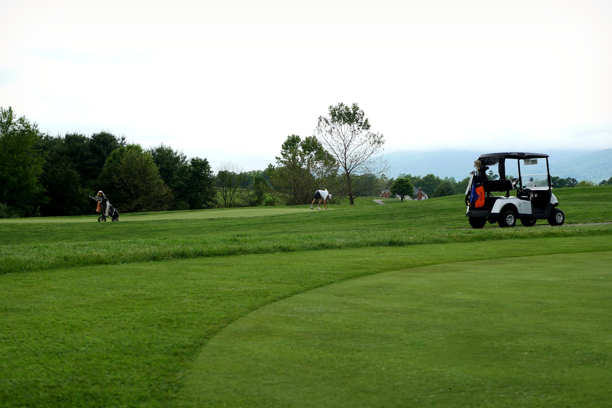 Golfers enjoying a day at a lush green golf course in Crozet, VA, under a cloudy sky.
