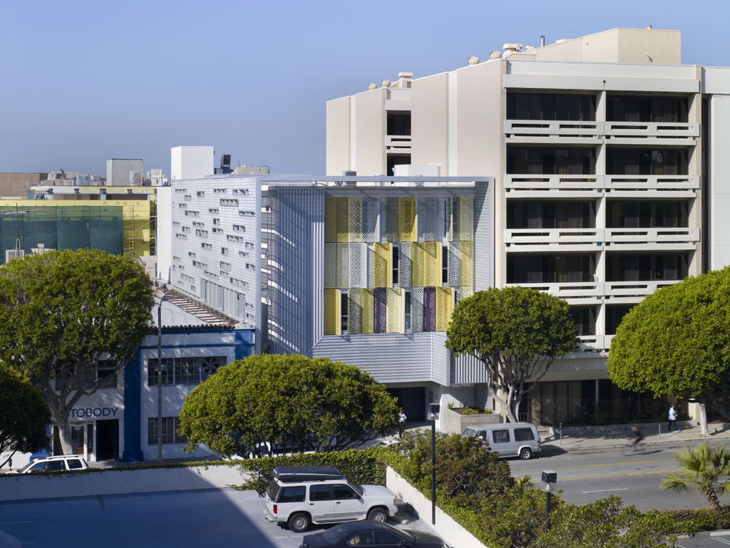 Multi-story affordable housing building with aluminum panel facade and street-level trees.